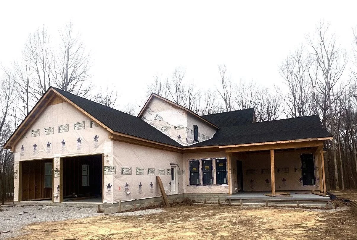 A house under construction with a black roof, unfinished exterior walls, and a porch.