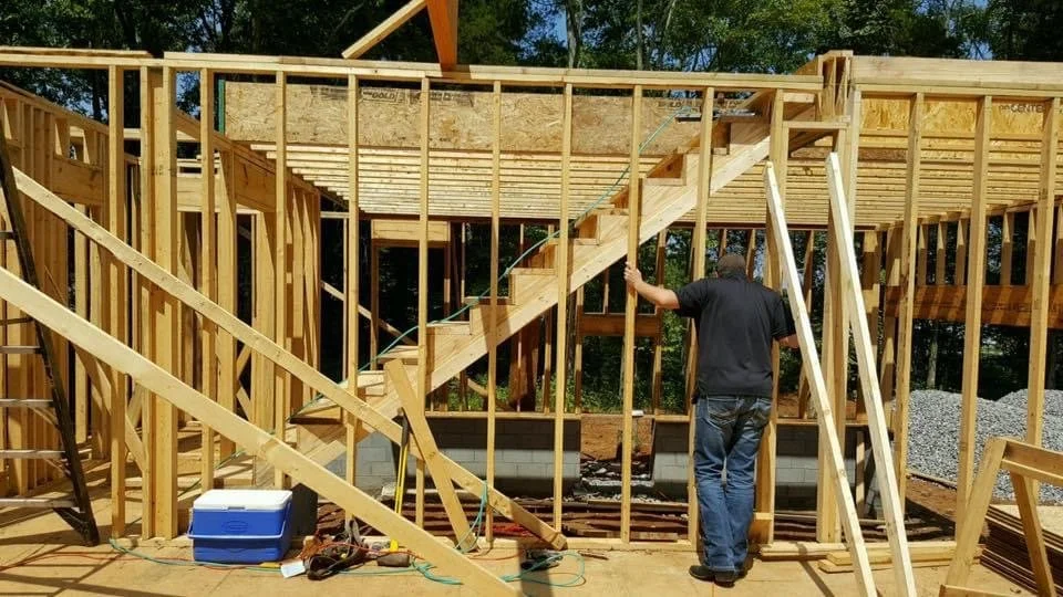 New Construction Investment with Take charge / Build for Profit owner on-site person working on the framing of a house under construction, with wooden walls and support beams.