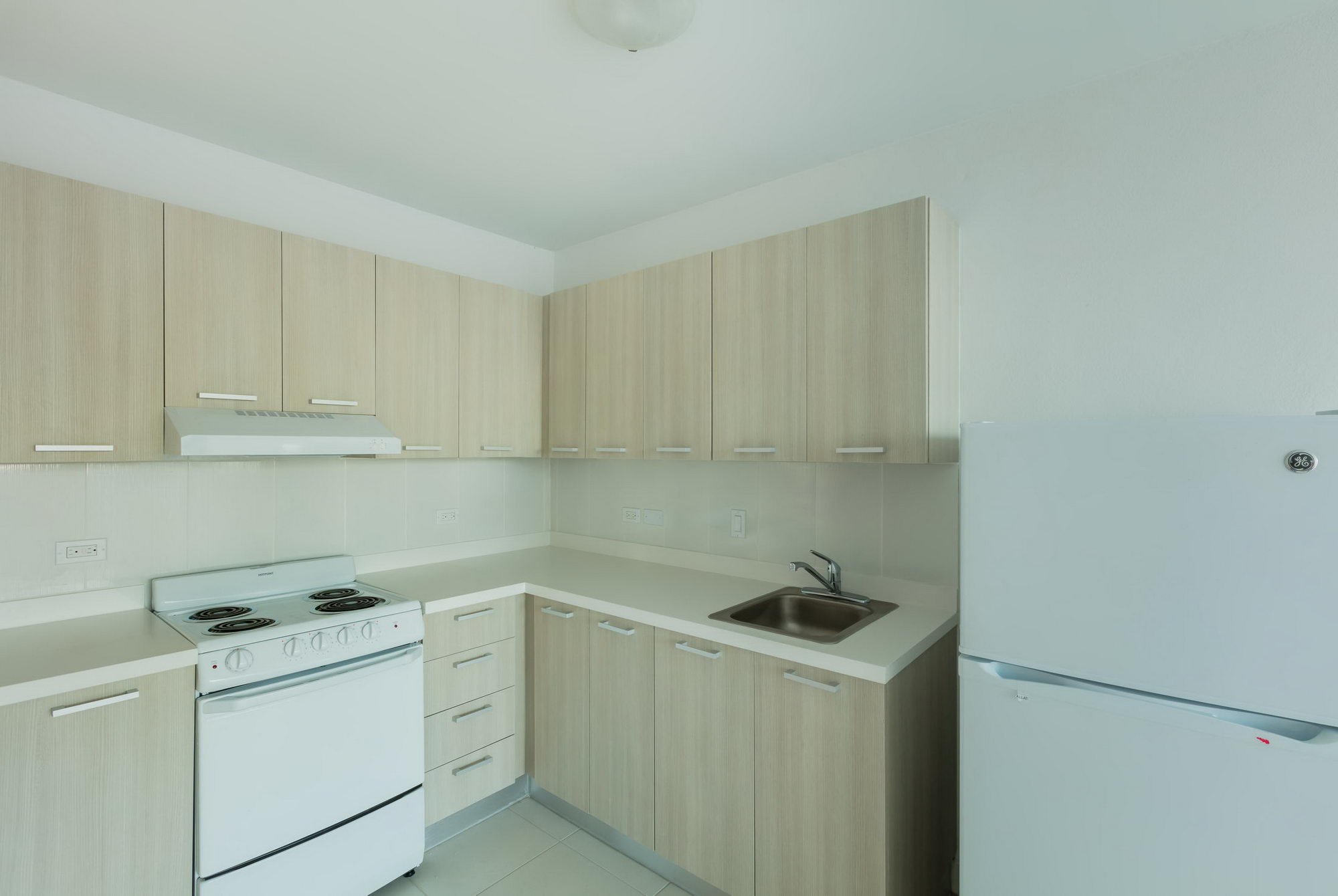 Kitchen with beige cabinets, white stove, sink, and refrigerator, minimal decor.