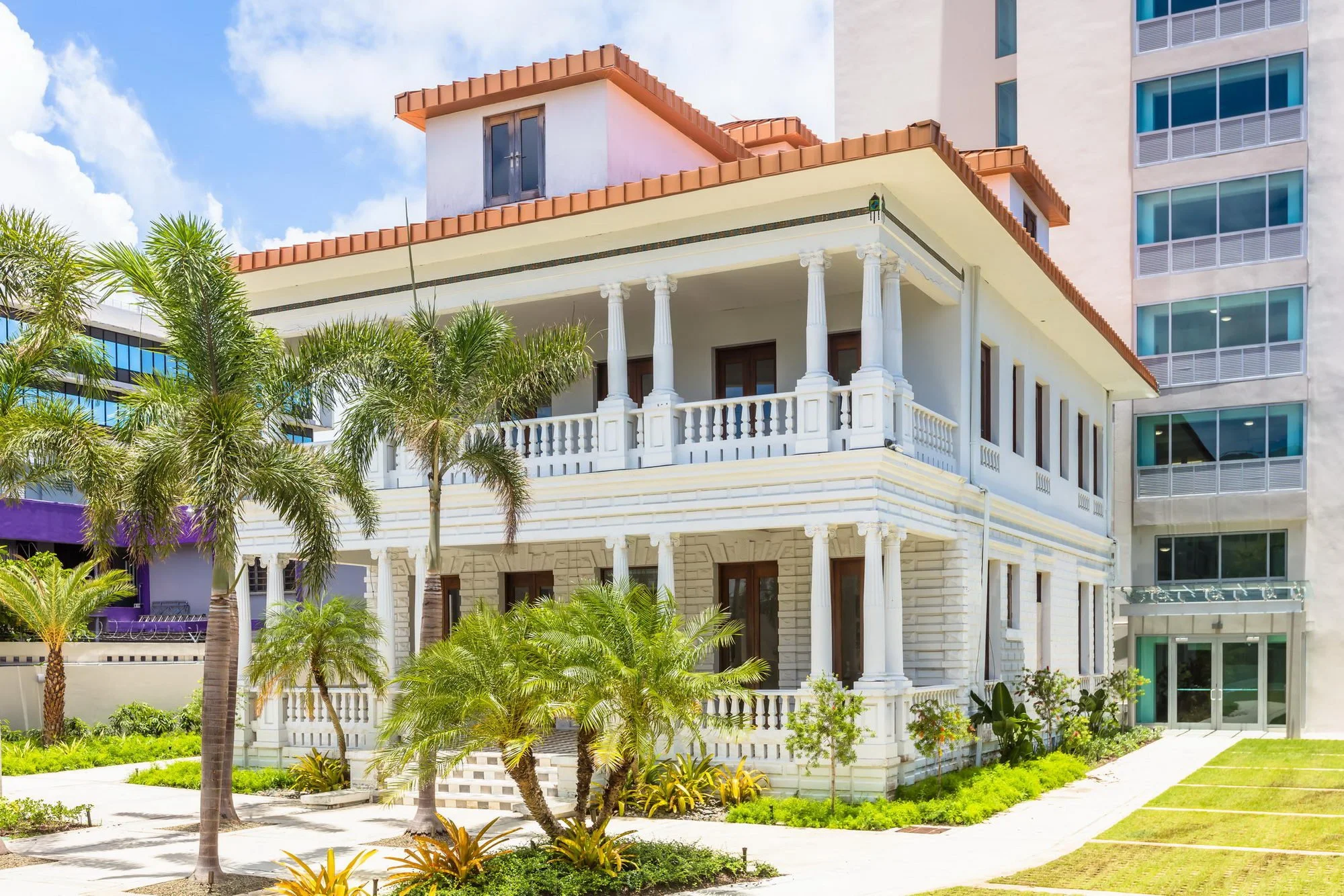Multi-story building with classical architectural design, columns, and a tropical landscaped area with palm trees in the foreground.