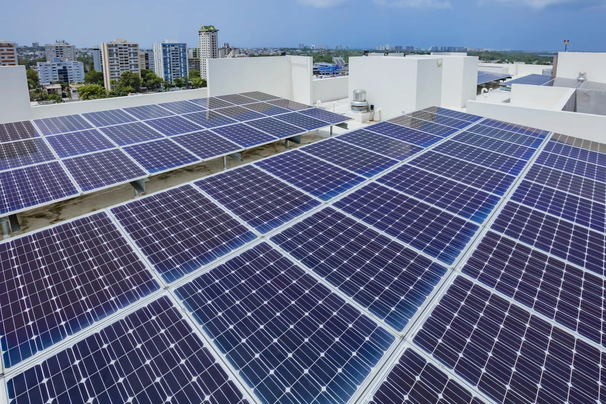 Roof with multiple solar panels installed, with a cityscape of high-rise buildings in the background.