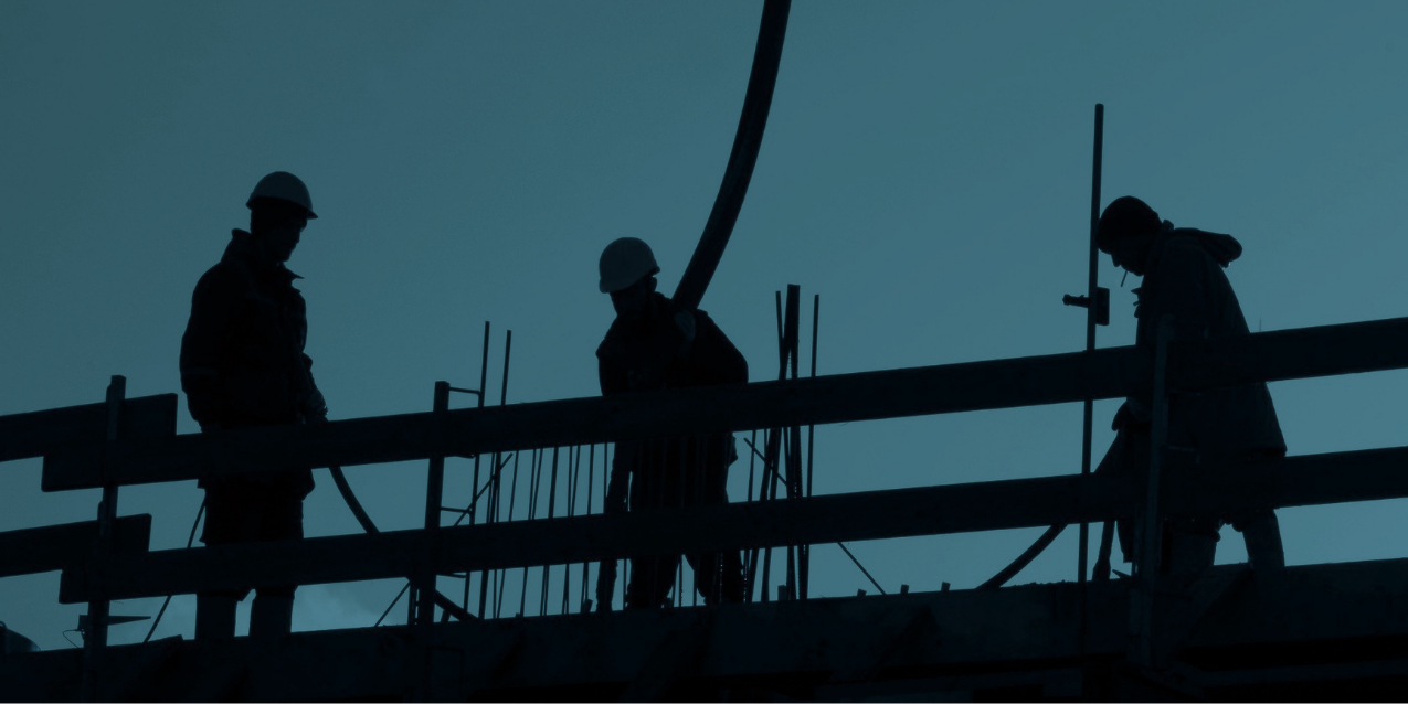 Silhouettes of three construction workers wearing helmets working on a building construction site.