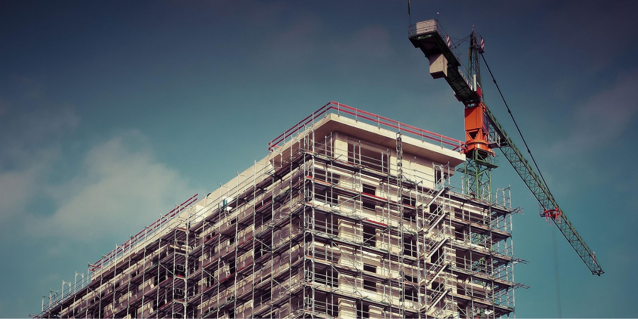 Construction site with scaffoldings around a high-rise building and a tower crane on the right side.
