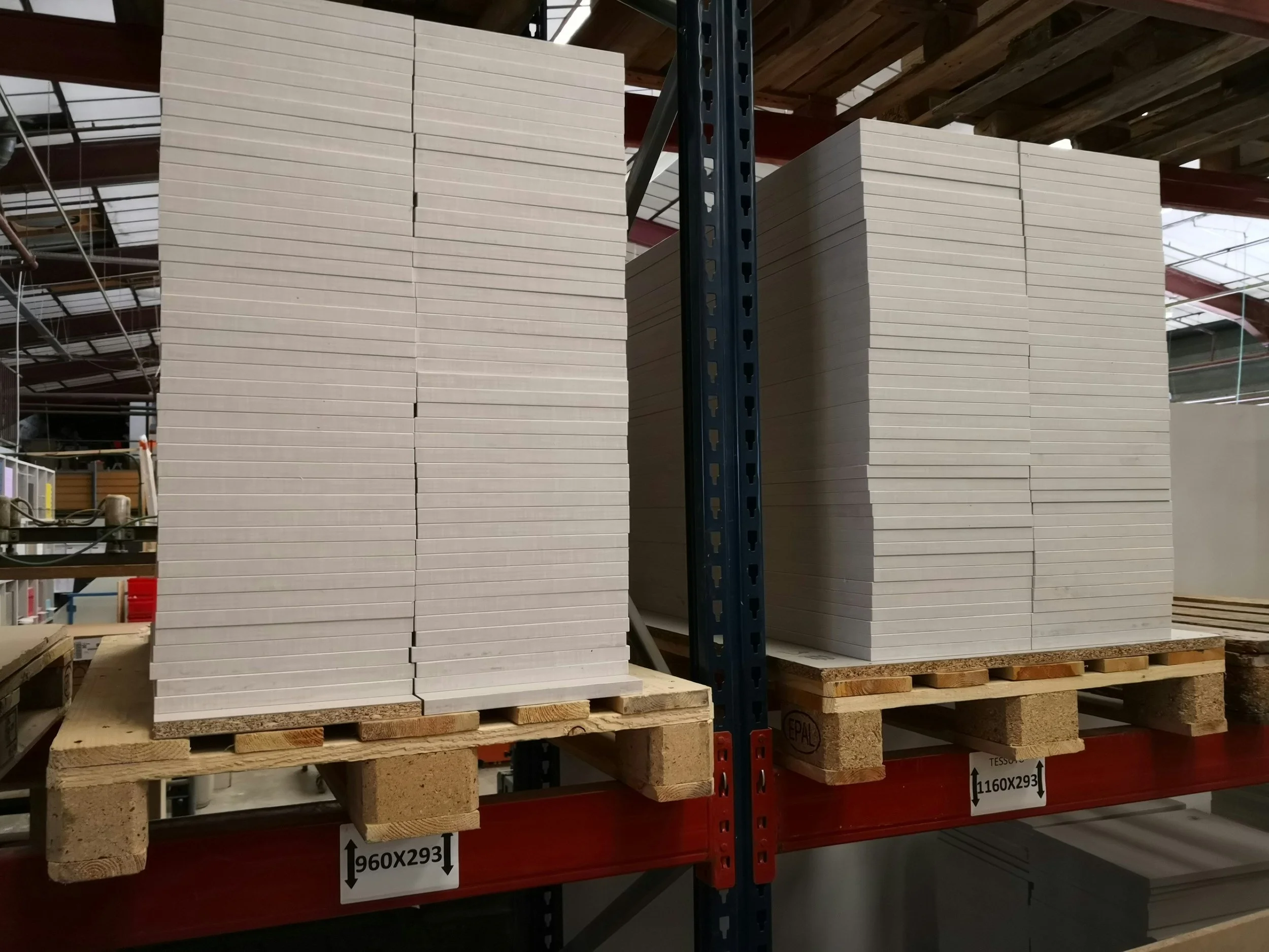 Stacks of large, grey board sheets on wooden pallets in a warehouse.