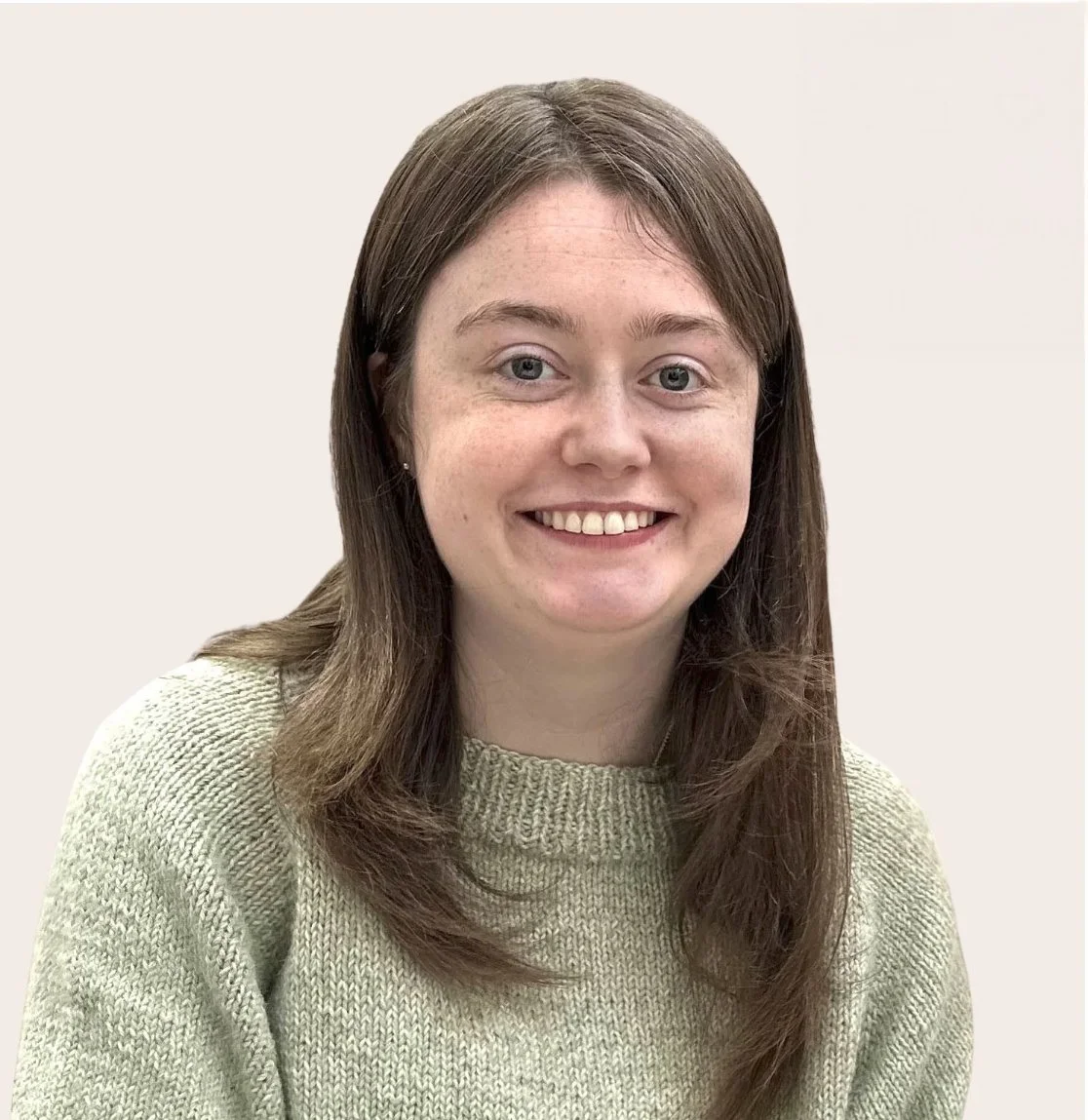 A young woman with shoulder-length brown hair, blue eyes, wearing a beige knitted sweater, smiling against a plain light background.