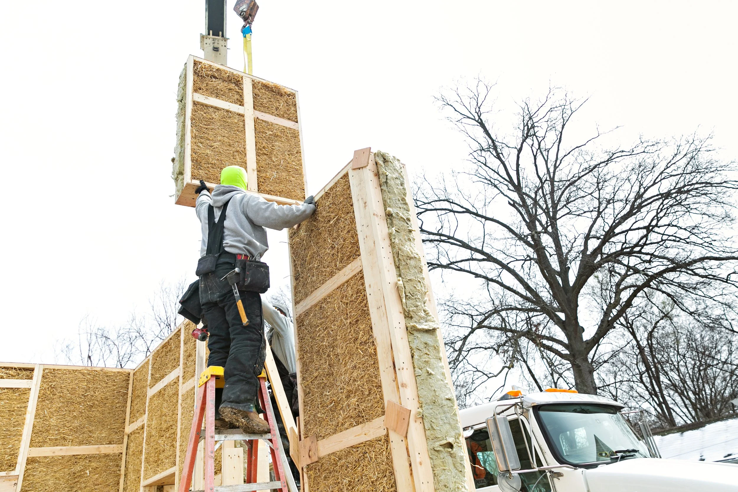 Building Integrity team executing precision prefabricated straw panel installation with boom truck crane demonstrating the speed and efficiency of panelized natural building construction