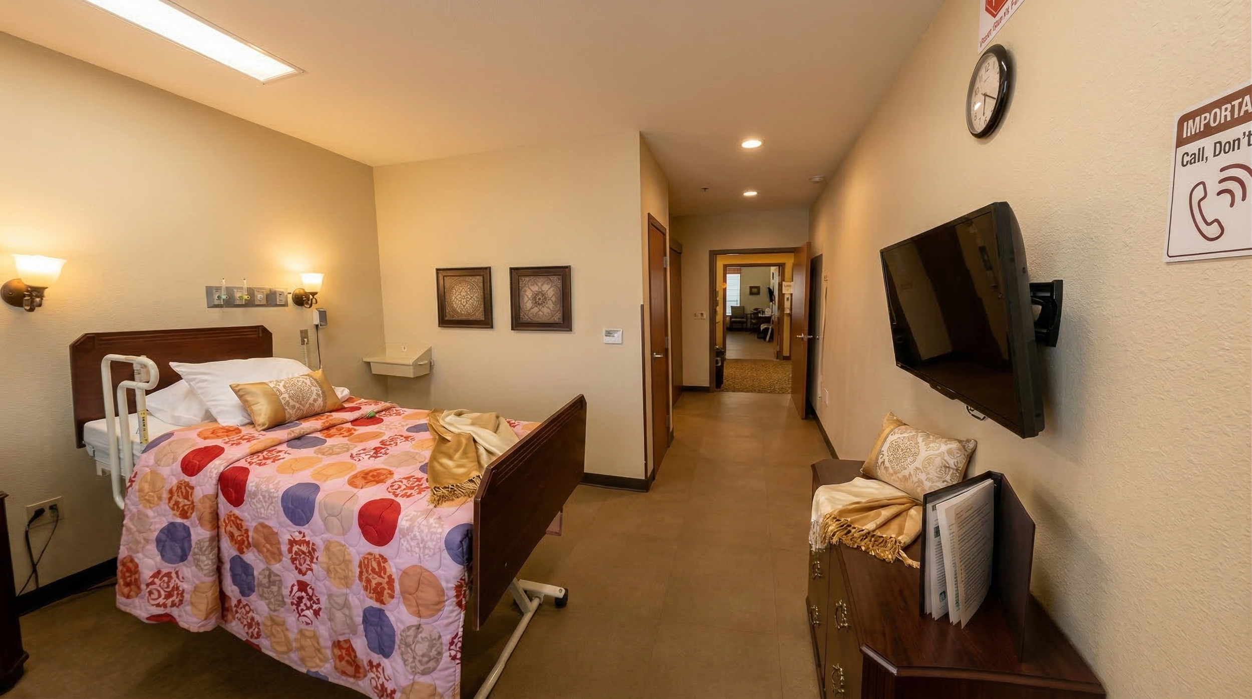 Senior assisted living suite with a bed, TV, hallway leading to other rooms, and decorative wall art.
