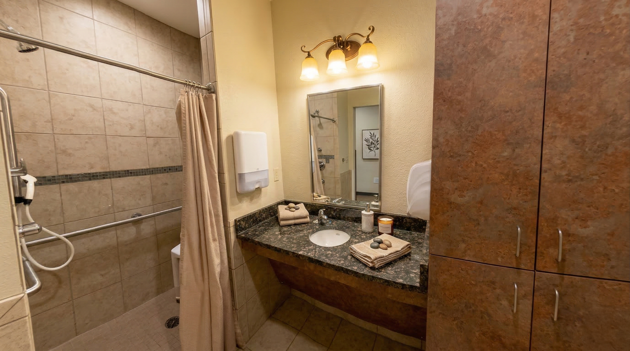 Private resident suite bathroom with shower, mirror, granite countertop, folded towels, soap, and cabinets.