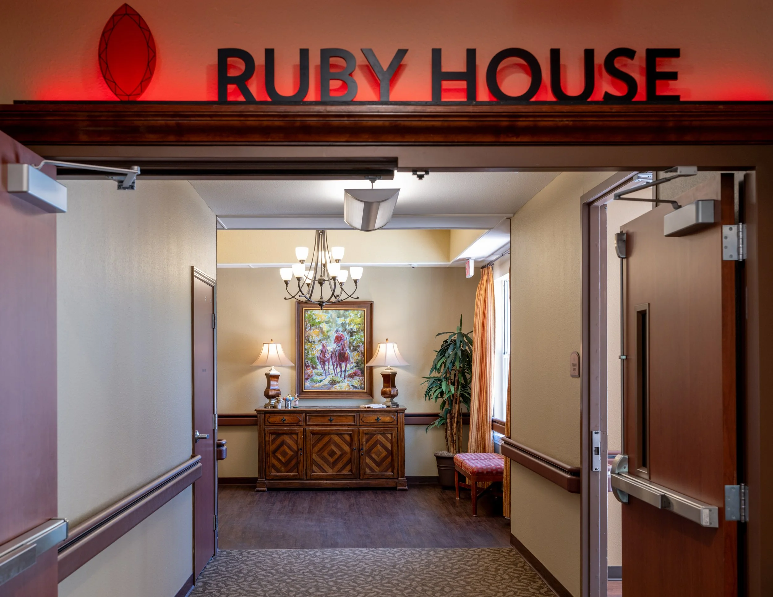 Interior hallway leading into a room at Ruby House, with beige walls, a wooden hutch, painted horse artwork, and warm lighting.