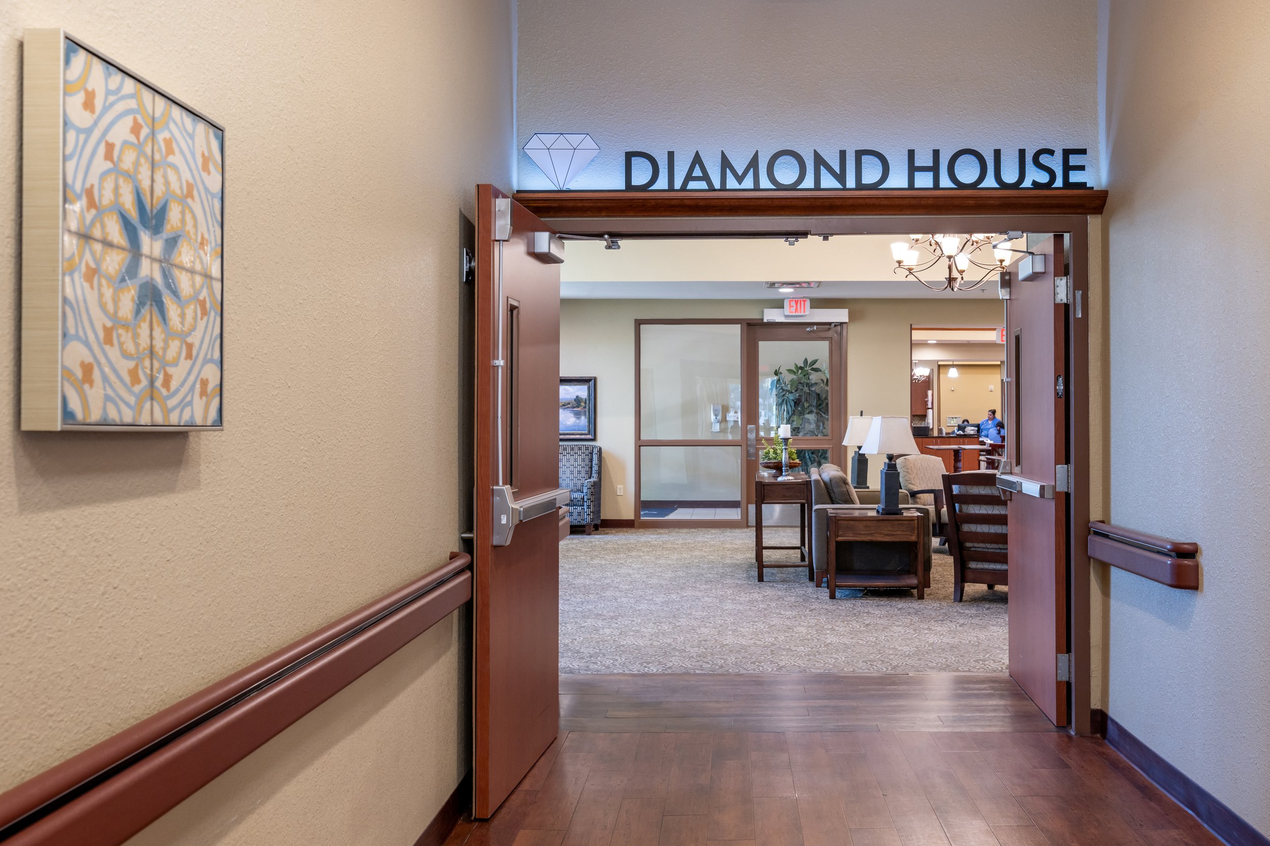 Entrance to the Diamond House lounge with open double doors leading into a seating area with chairs, sofas, a lamp, and a chandelier, and a sign above the doorway reading 'DIAMOND HOUSE' with a diamond icon.