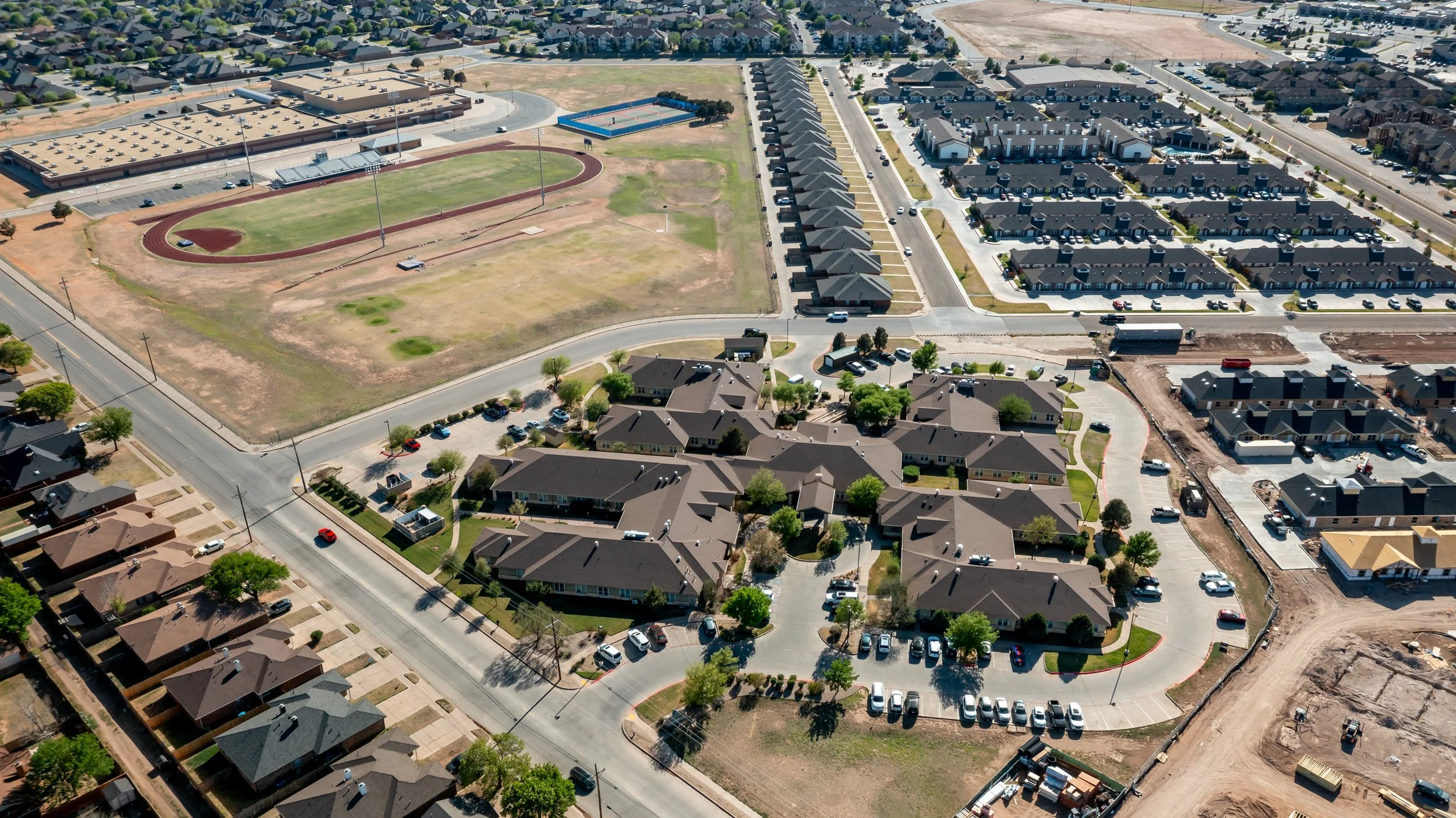 Aerial view of a nursing home around a neighborhood with houses, a sports field, and ongoing construction.