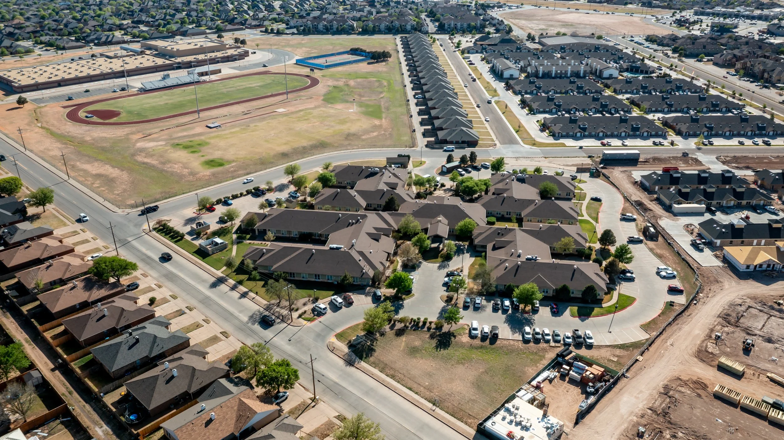 Aerial view of a nursing home in Lubbock with a sports field and residential houses, showing ongoing construction.