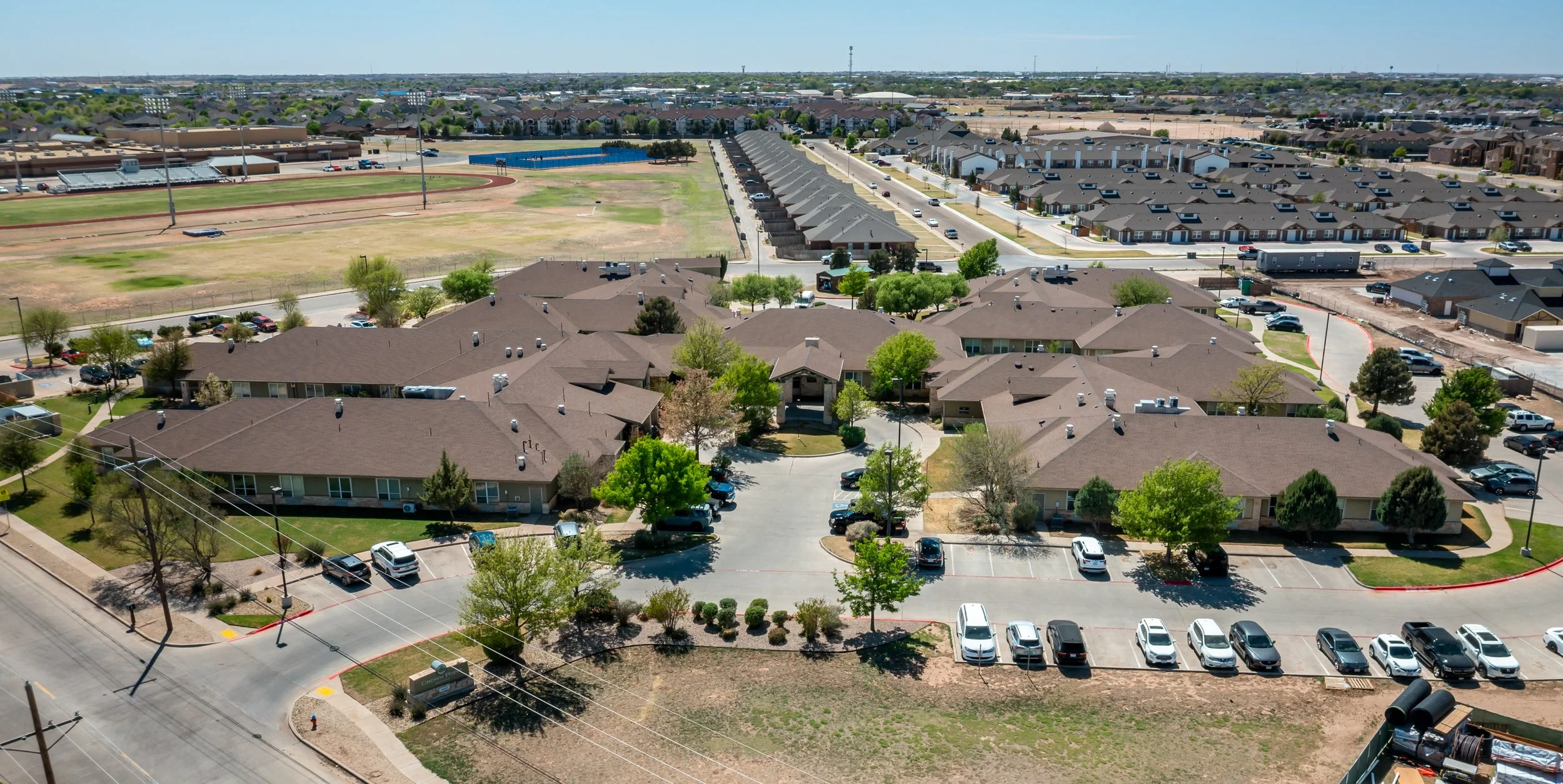 Aerial view of Lubbock Nursing Home with parking lots, surrounded by trees, nearby sports field, and housing developments.