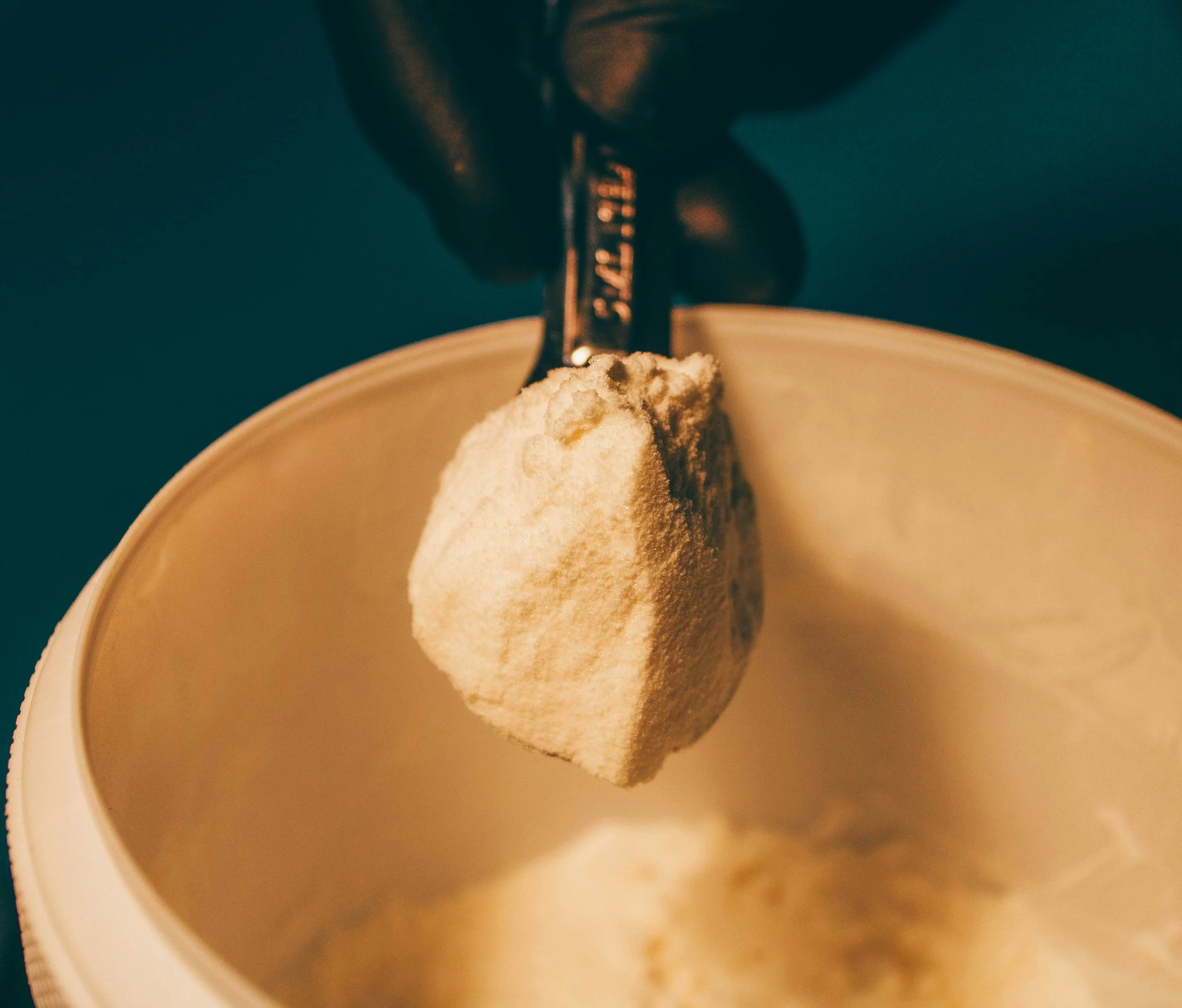 Close-up of a spoon pressing into a scoop of vanilla ice cream in a bowl, against a dark background.