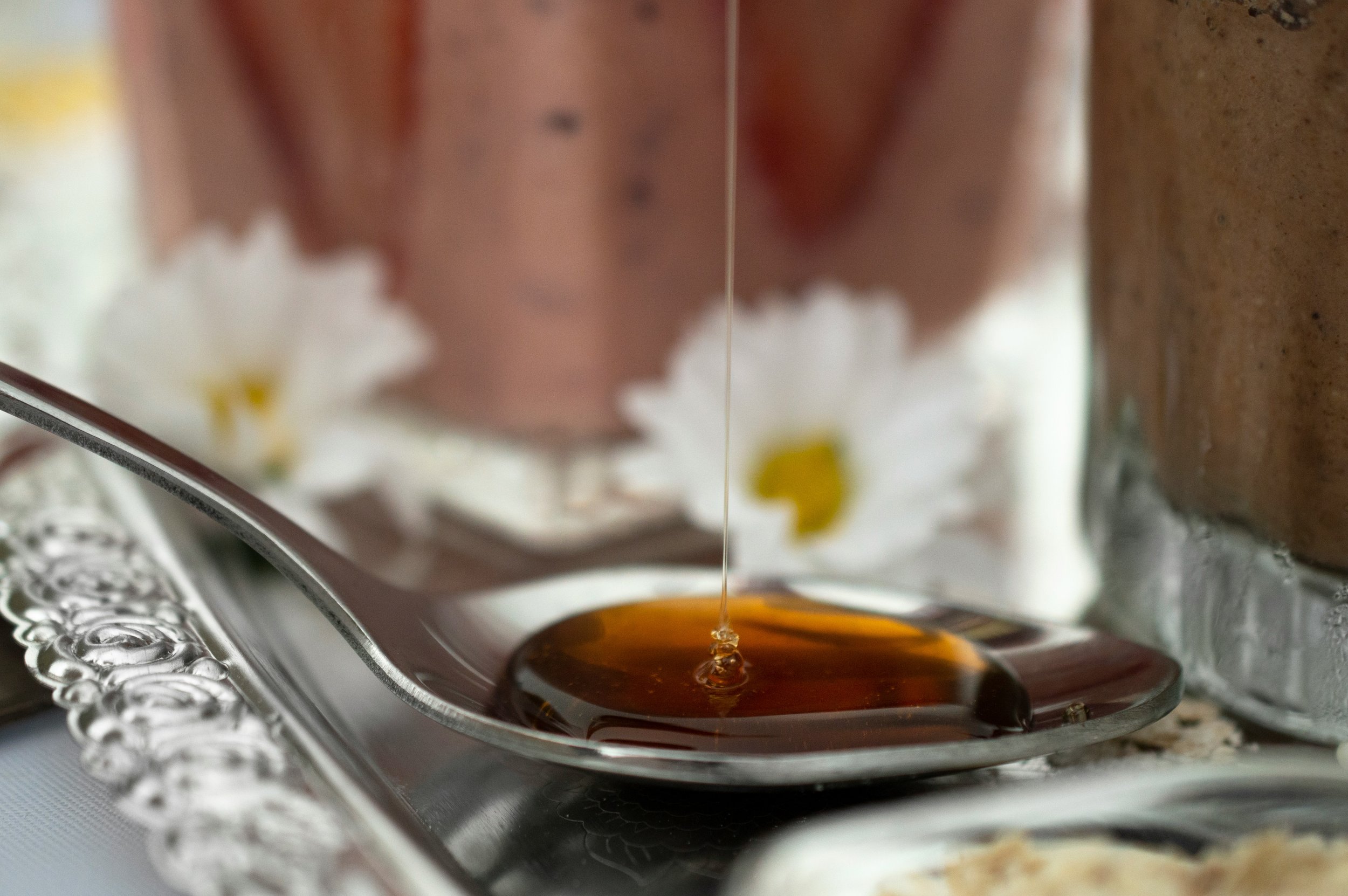 Close-up of honey being poured into a jar from a glass honey dipper.
