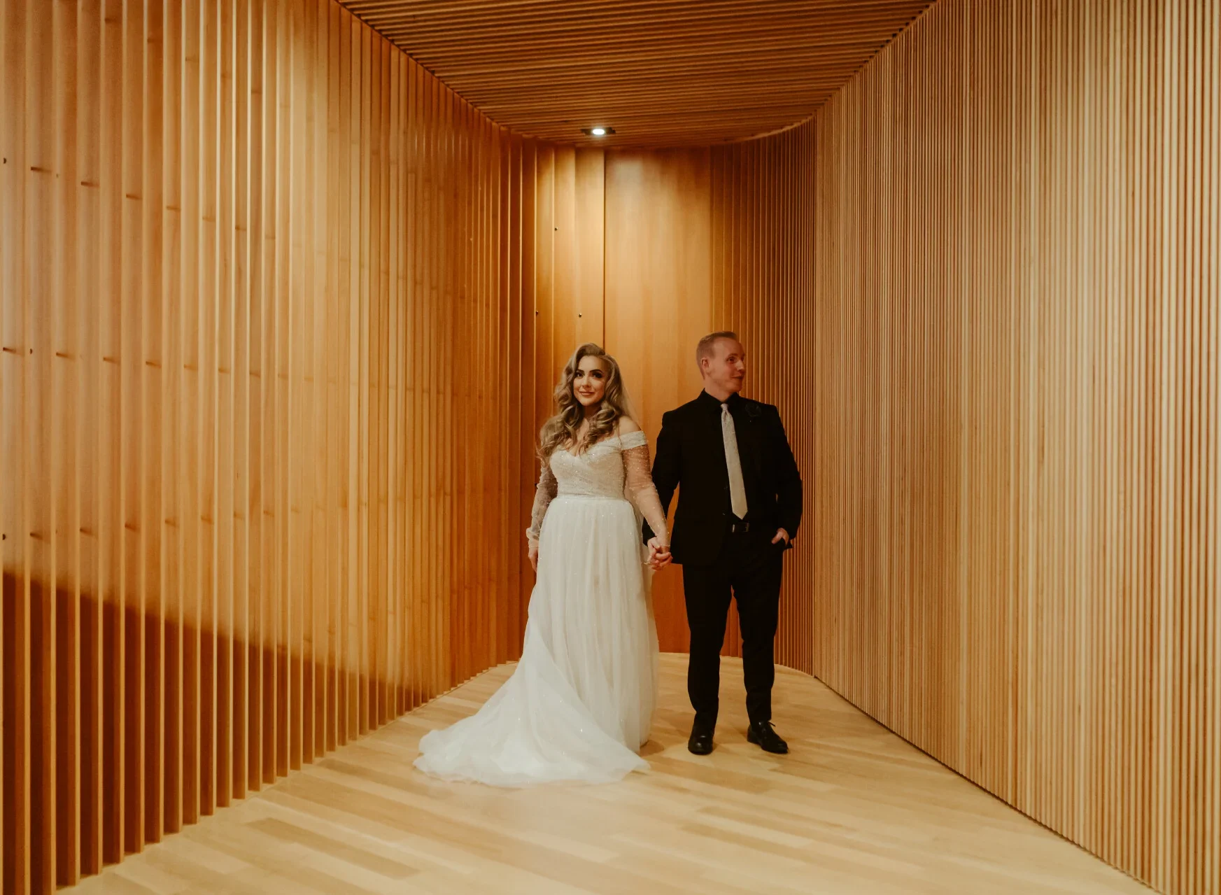 A bride and groom holding hands in a wooden hallway.