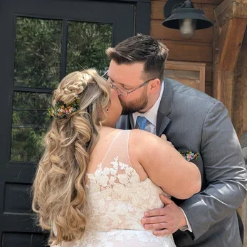 Modern building with large glass window, wooden siding, located in a mountainous area with sparse vegetation and a mountain range in the background.