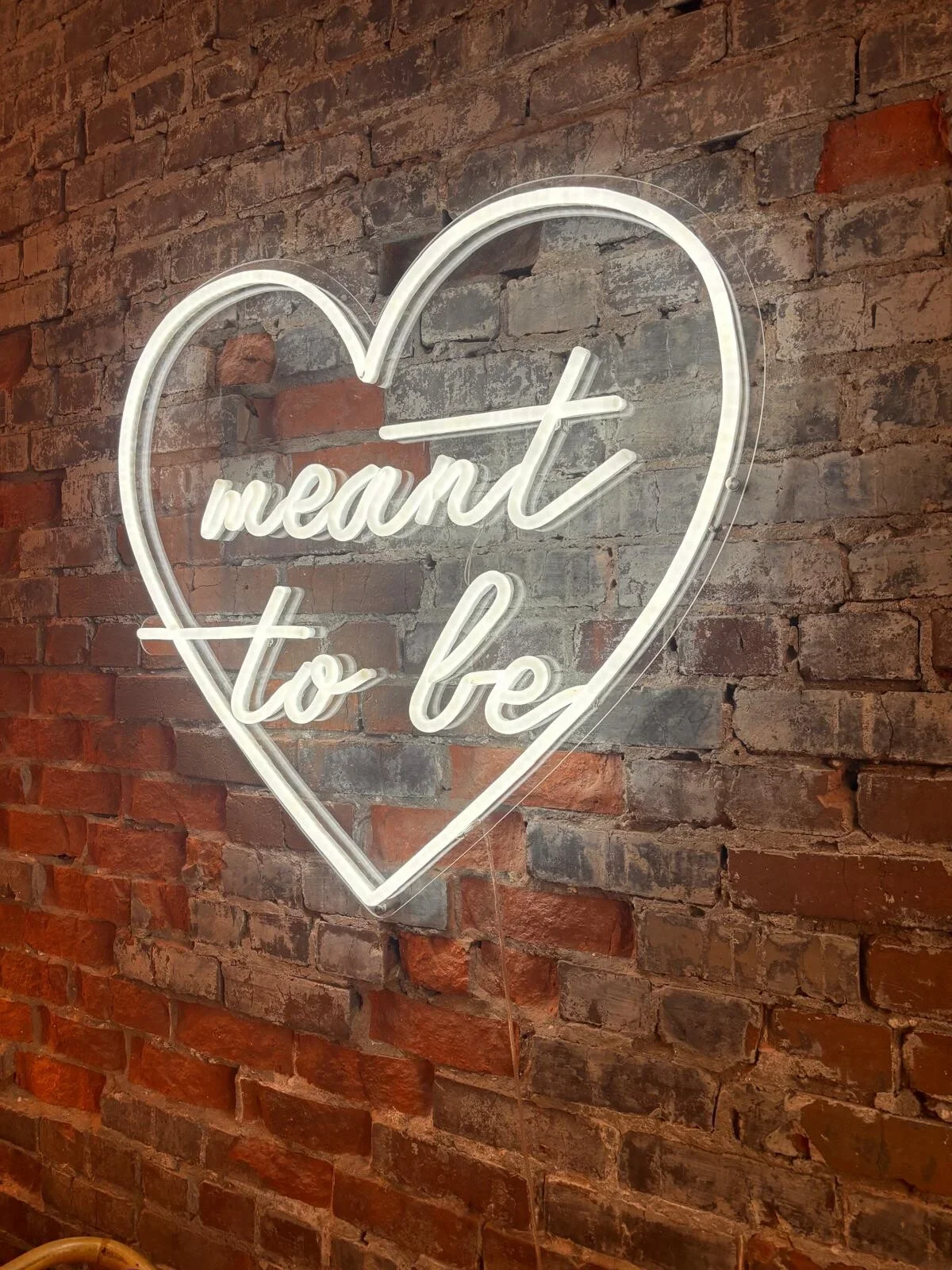 Neon sign with the words "heart to be" inside a heart outline on a brick wall.