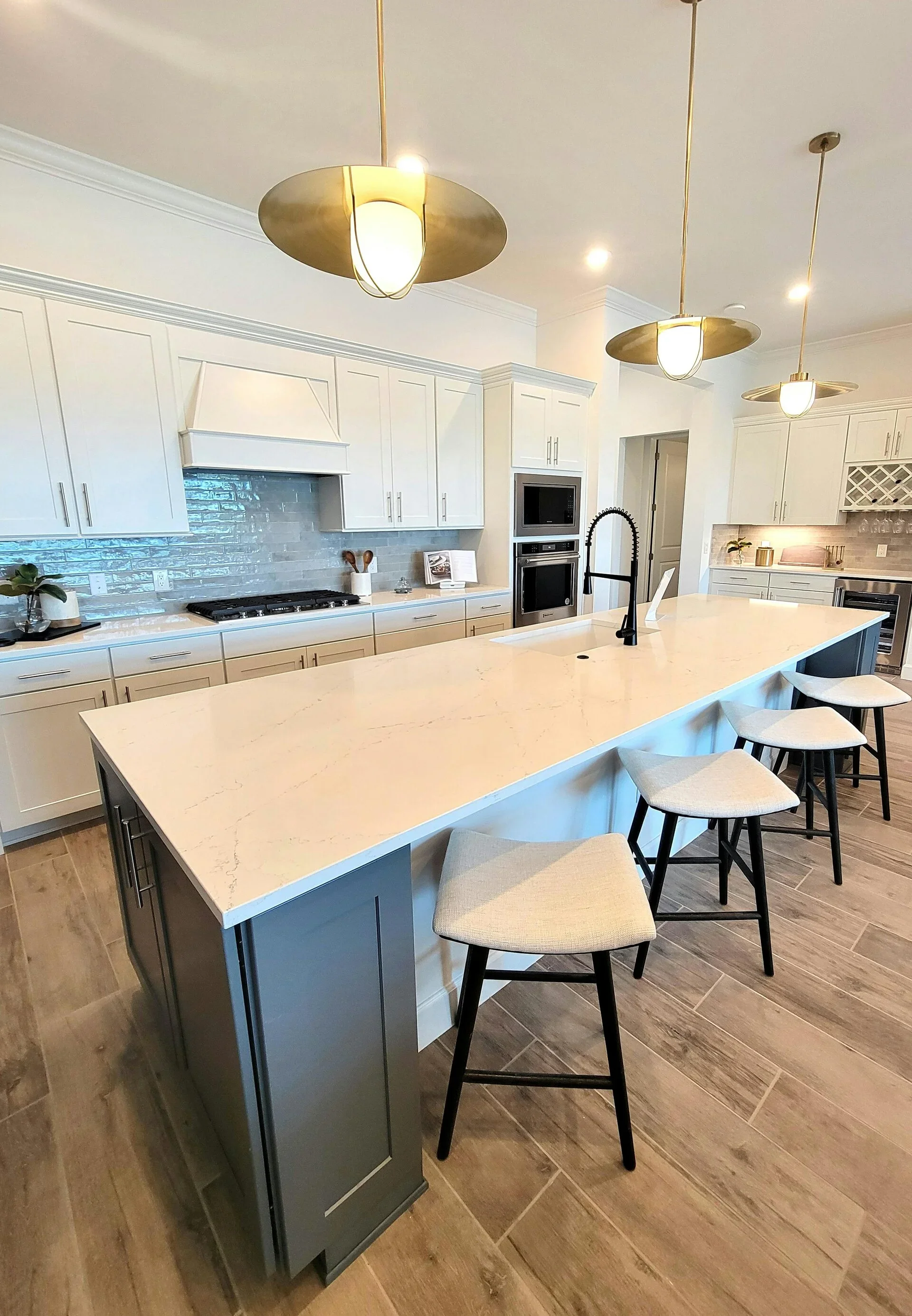 Modern kitchen with white cabinets, a large island with a white marble countertop, black bar stools, pendant lights, a black faucet, and stainless steel appliances.