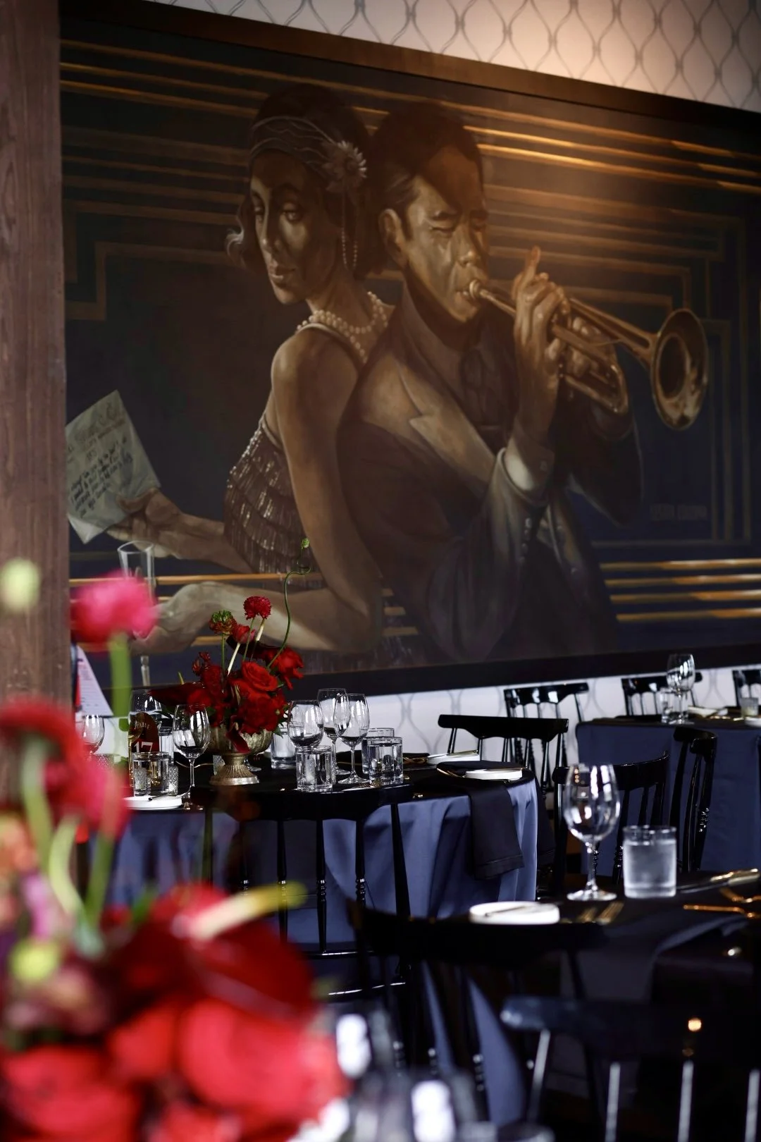 Interior of The Birmingham with a its large wall mural featuring a jazz musician playing the trumpet and a woman in a 1920s flapper dress holding a newspaper, with tables set for a formal special event.