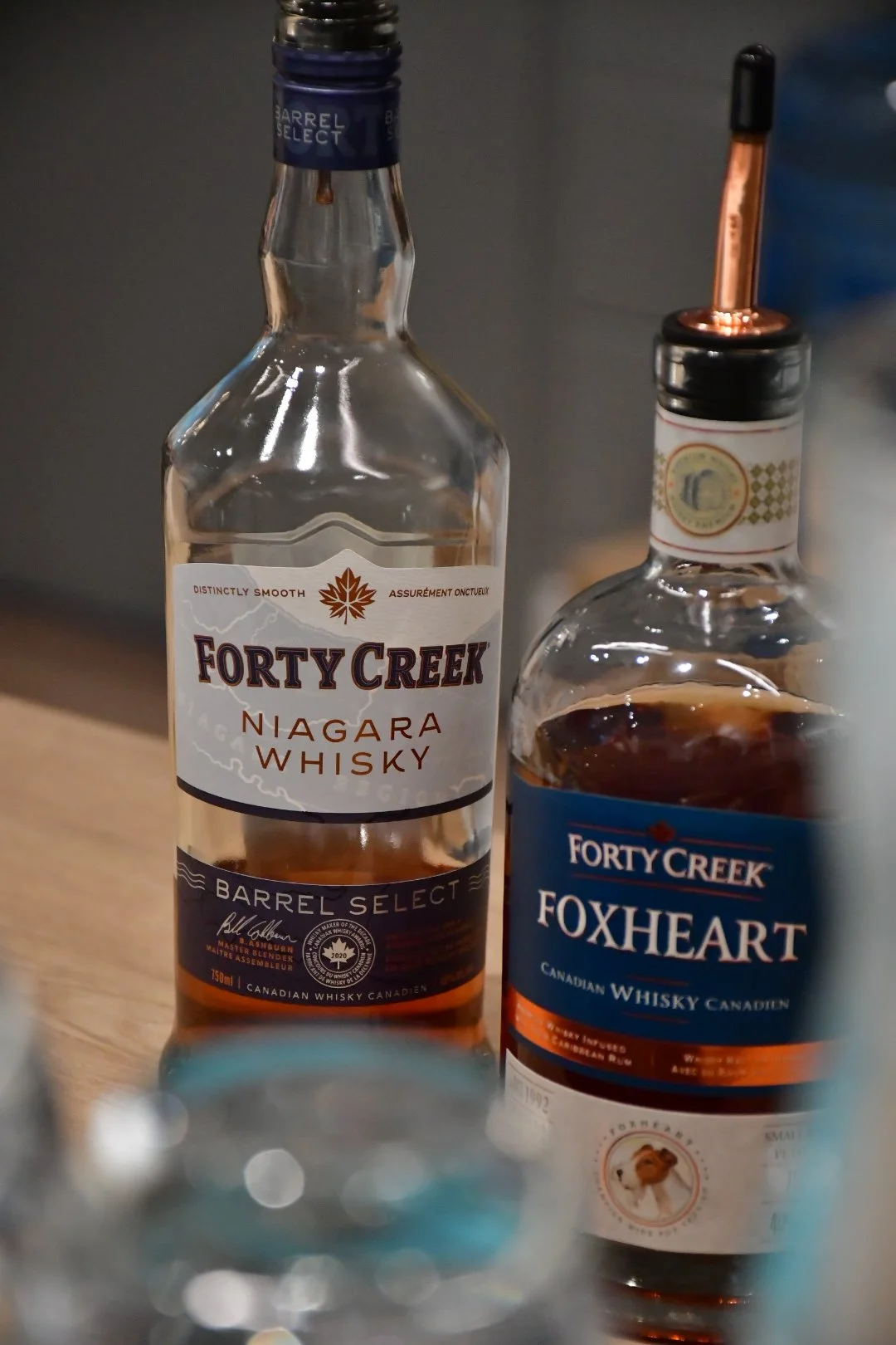 Two bottles of whiskey, one labeled 'Forty Creek Niagara Whisky' and the other labeled 'Forty Creek Foxheart Canadian Whisky,' placed on a bar.