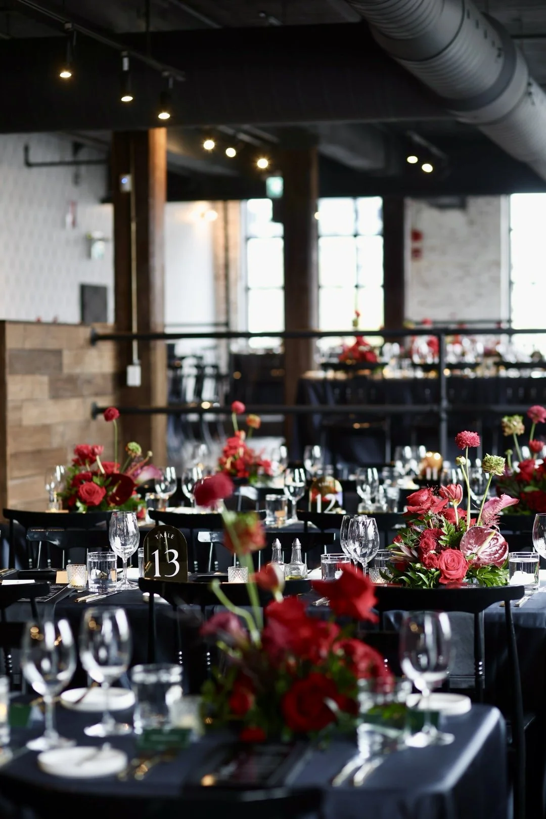 The Birmingham's elegant indoor event space decorated with red floral arrangements, set with wine glasses, water glasses, and tableware, with tables numbered for seating.