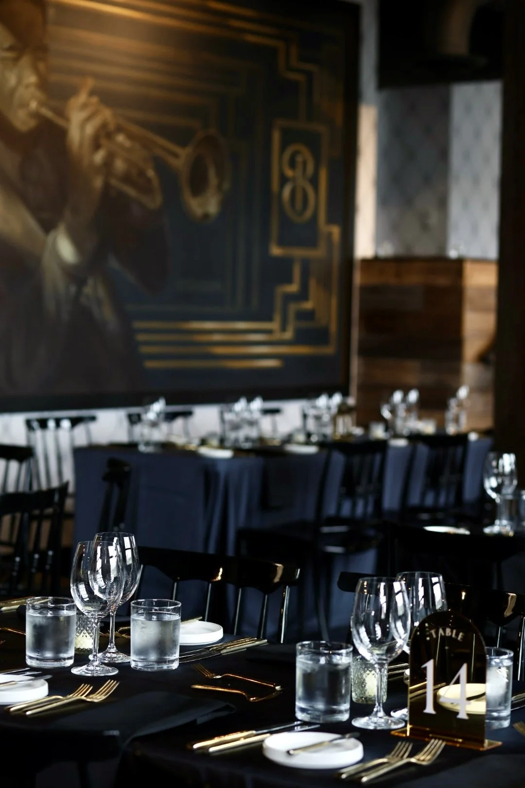 The Birmingham interior set up for a special event with black tablecloths, glassware, plates, gold-colored cutlery, and a table number sign indicating table 14. The overall decor is sophisticated and modern.