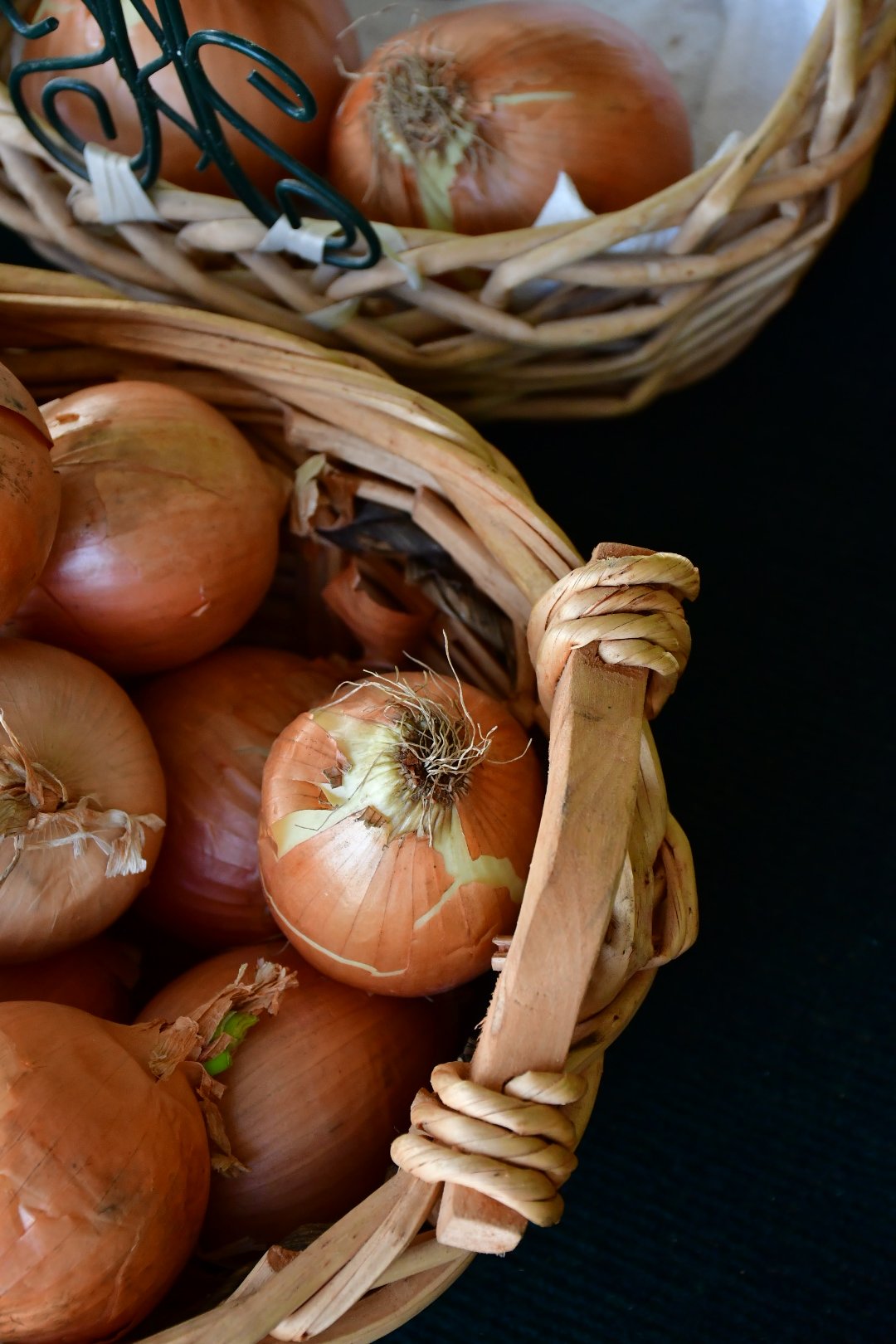 Onions in woven basket on dark surface.