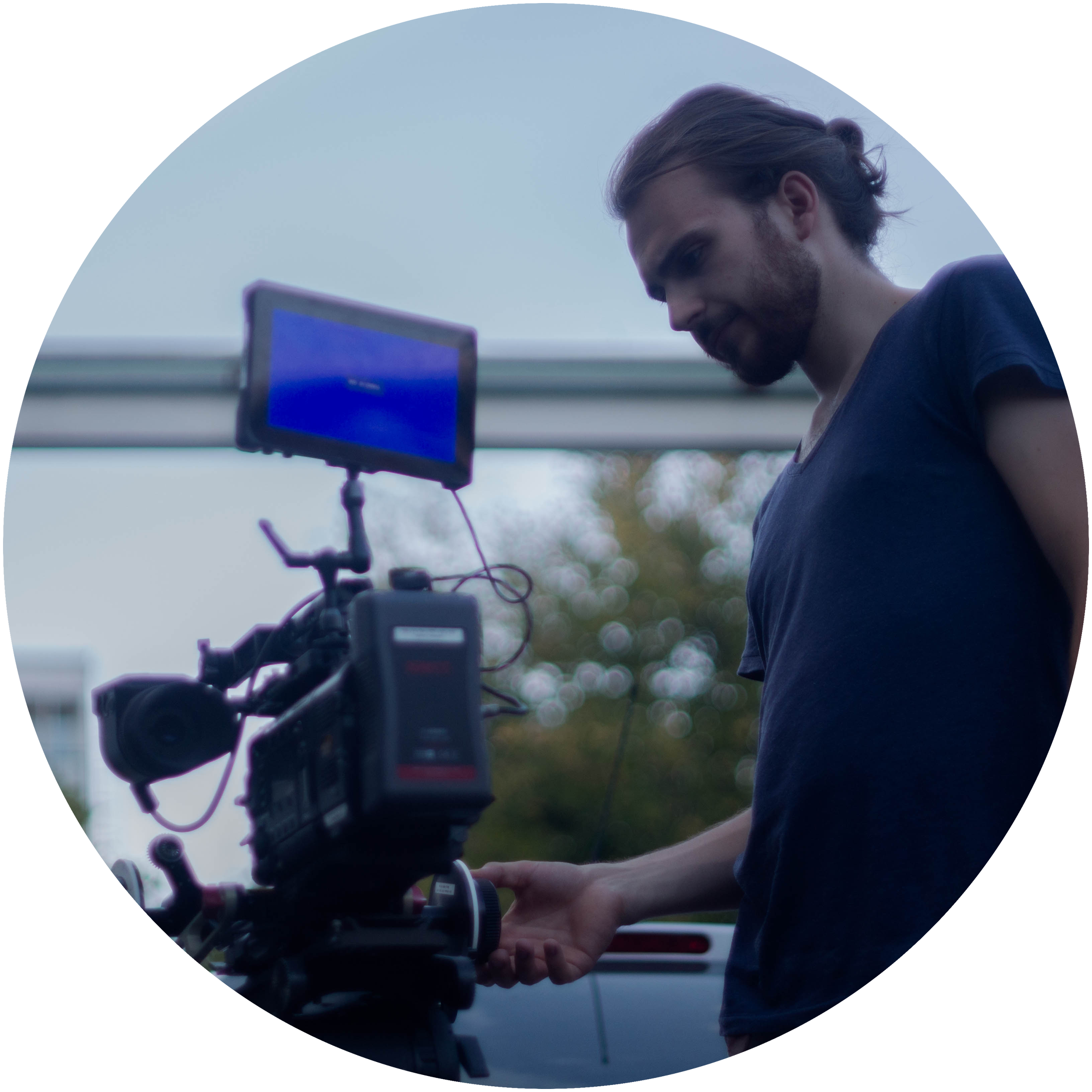 Antoine Matuttis - A young man with brown hair and a beard is working with a cinema camera outdoors, with a cloudy sky in the background.