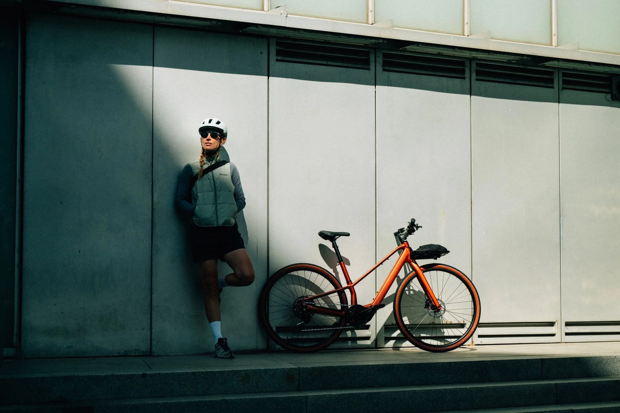 Frau in Fahrradhelm und Sportkleidung lehnt an einer Wand, neben Fahrrad