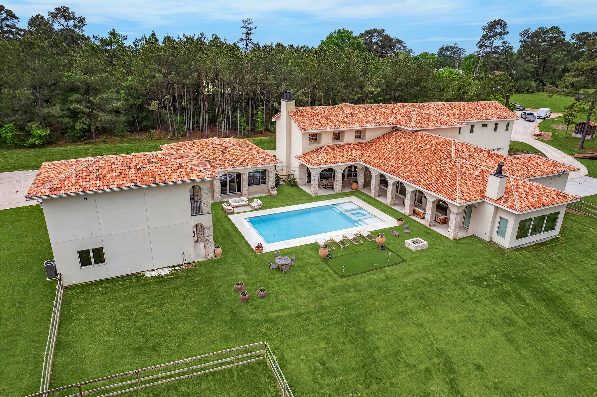 A large house with a red tile roof, a swimming pool in the backyard, and lush green lawn surrounded by trees.