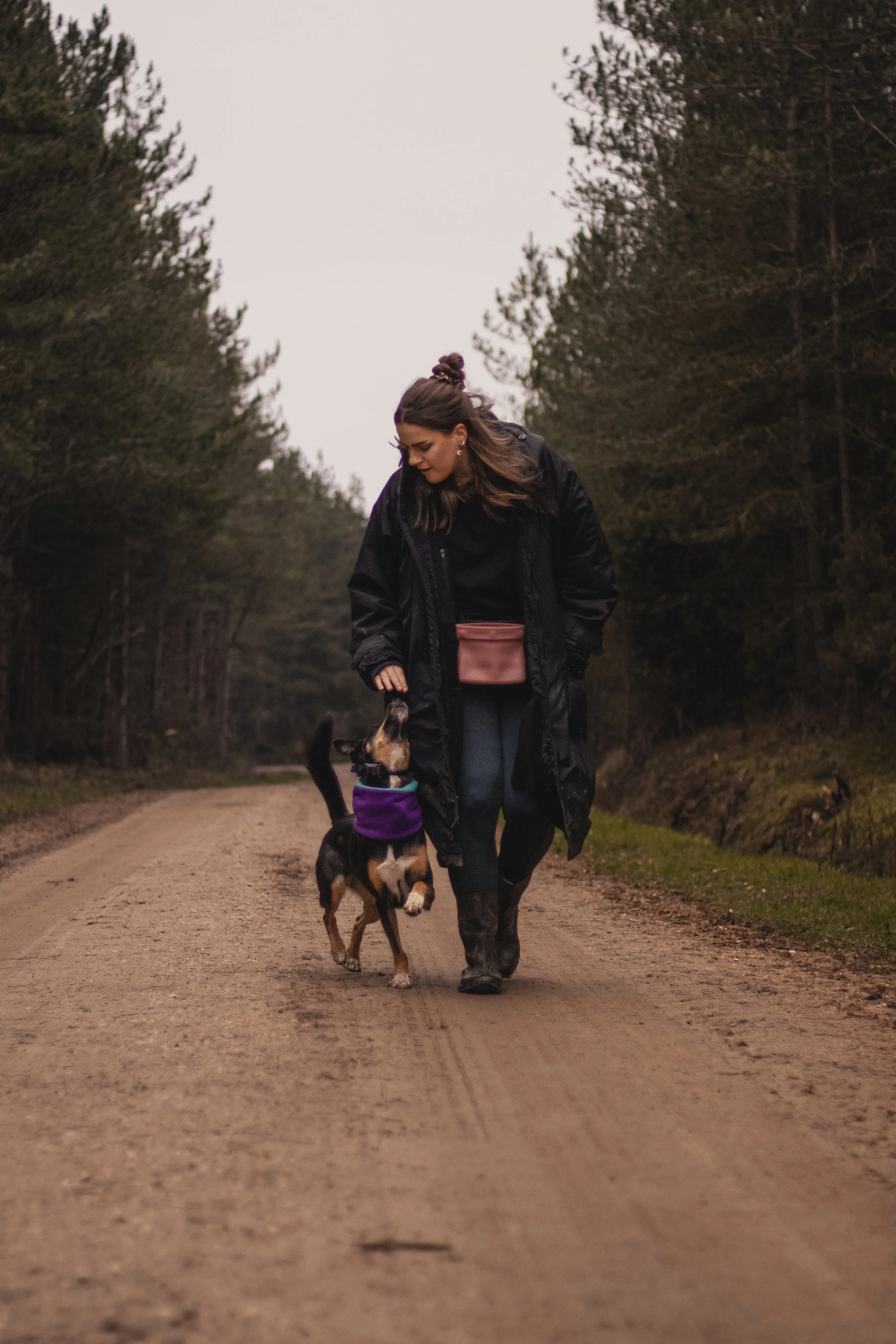 Woman walking her dog on a dirt path in a wooded area.