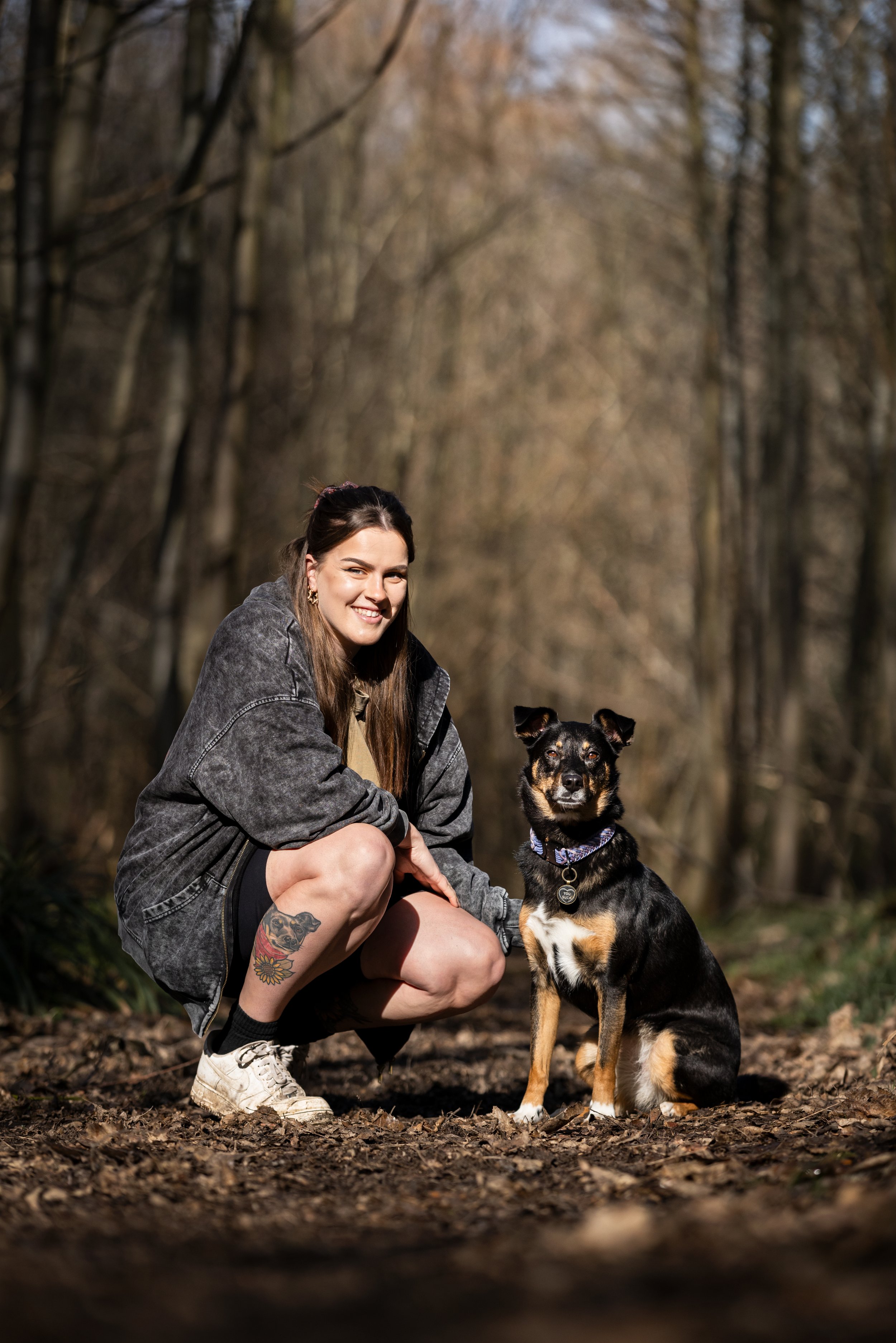 A woman squatting in a forest with a black and tan dog sitting beside her.
