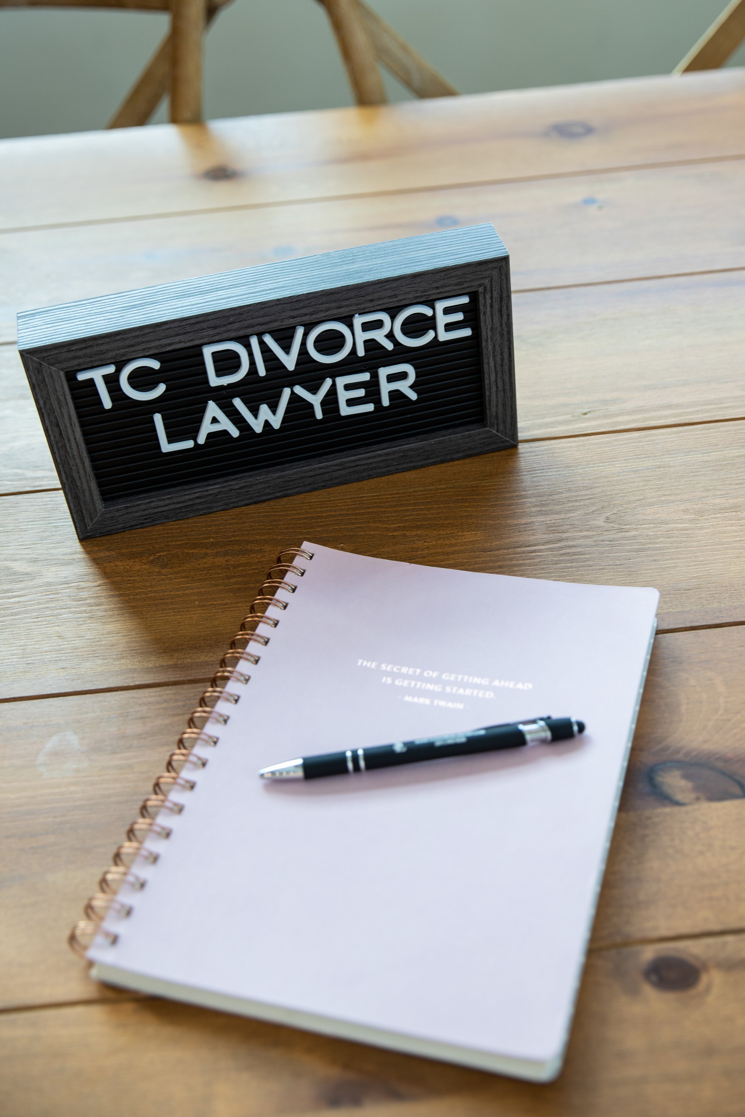 A desk with a sign reading "TC Divorce Lawyer," a pink notebook with a quote, and a black pen.
