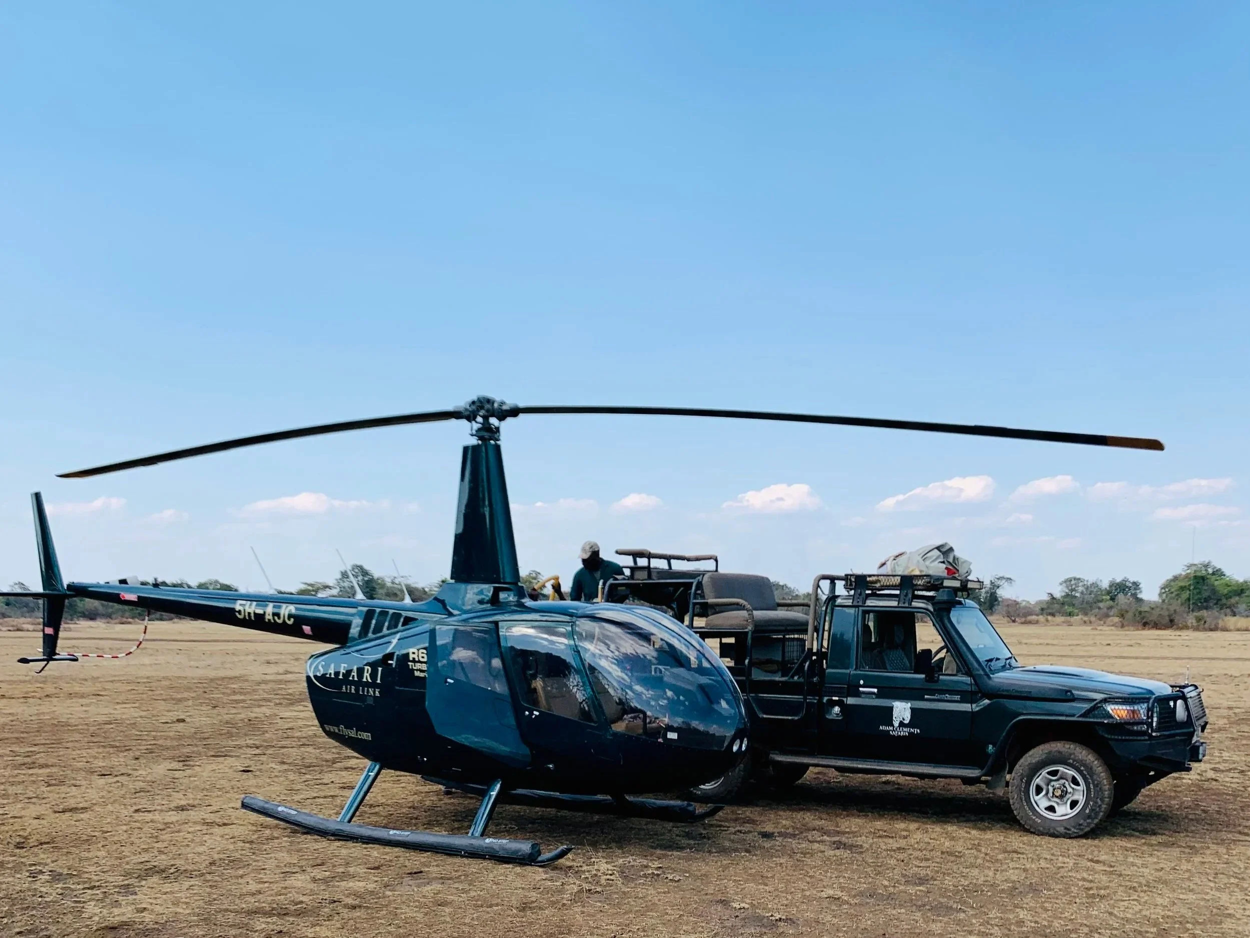 A helicopter and a black vehicle parked on a dry grass field under a clear blue sky with some clouds.