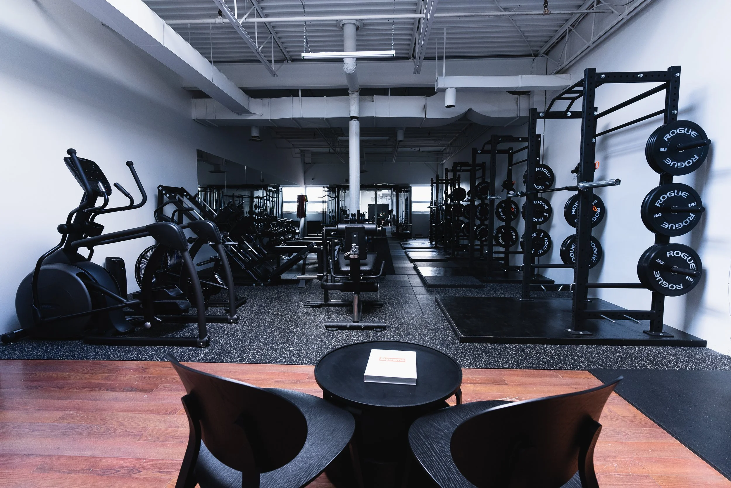 Empty gym with exercise equipment, weight rack, and chairs in foreground.