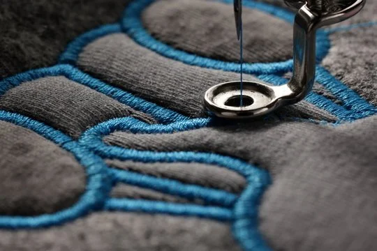 Close-up of a sewing machine needle stitching blue thread onto gray fabric.