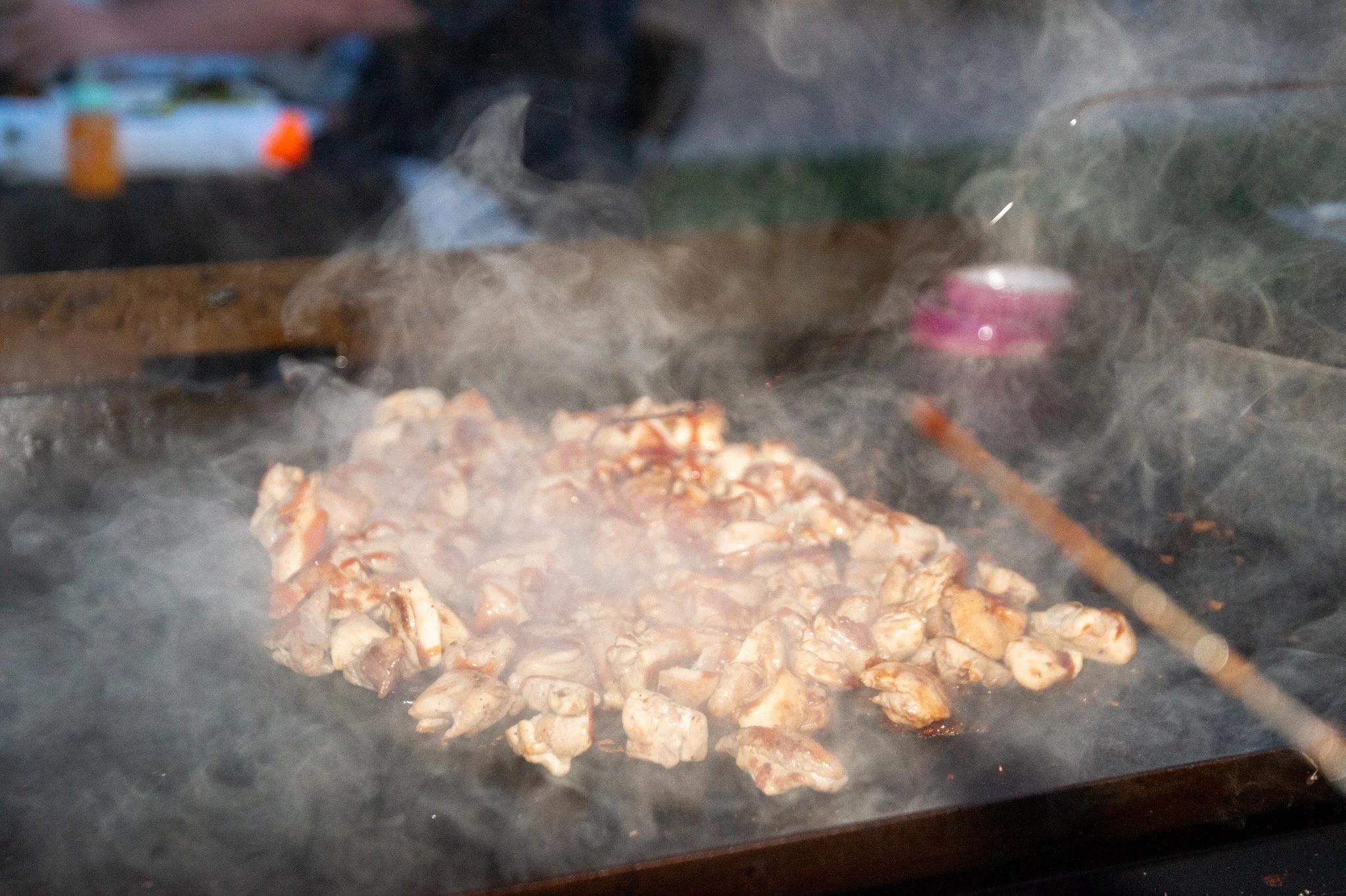 Chunks of meat cooking on a hot griddle with steam or smoke rising.
