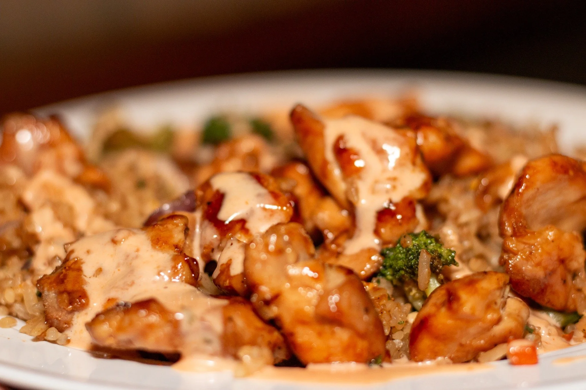 Close-up of saucy chicken pieces served over rice with broccoli and other vegetables on a white plate.