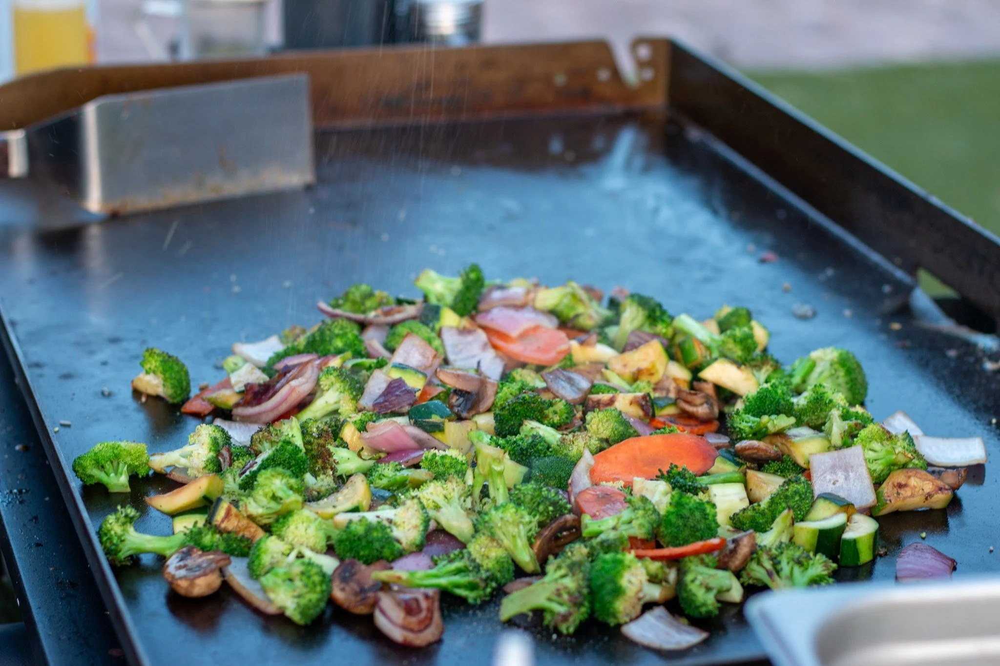 Sautéed mixed vegetables including broccoli, mushrooms, carrots, zucchini, and onions on a black electric griddle.