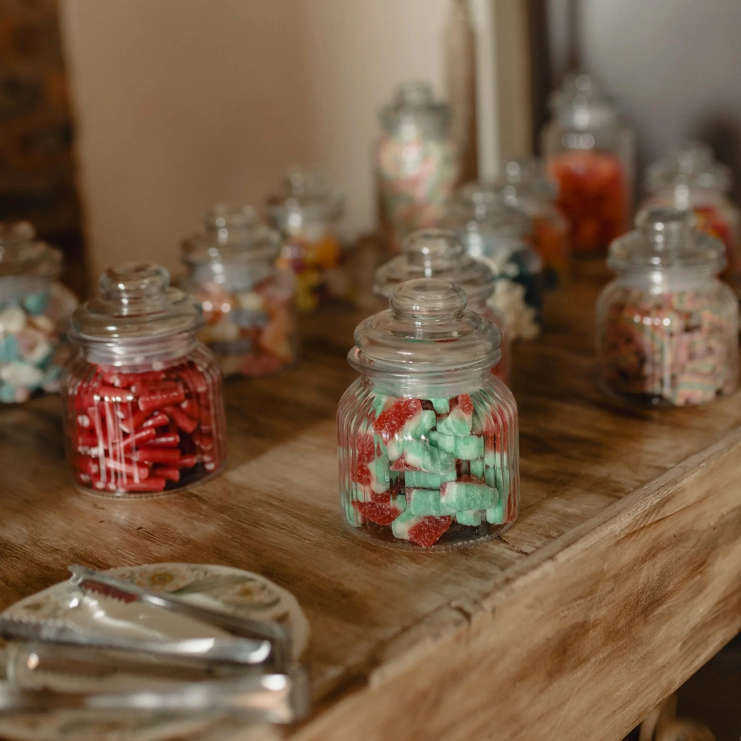 Close-up of glass jars filled with colorful candies, placed on a wooden surface.
