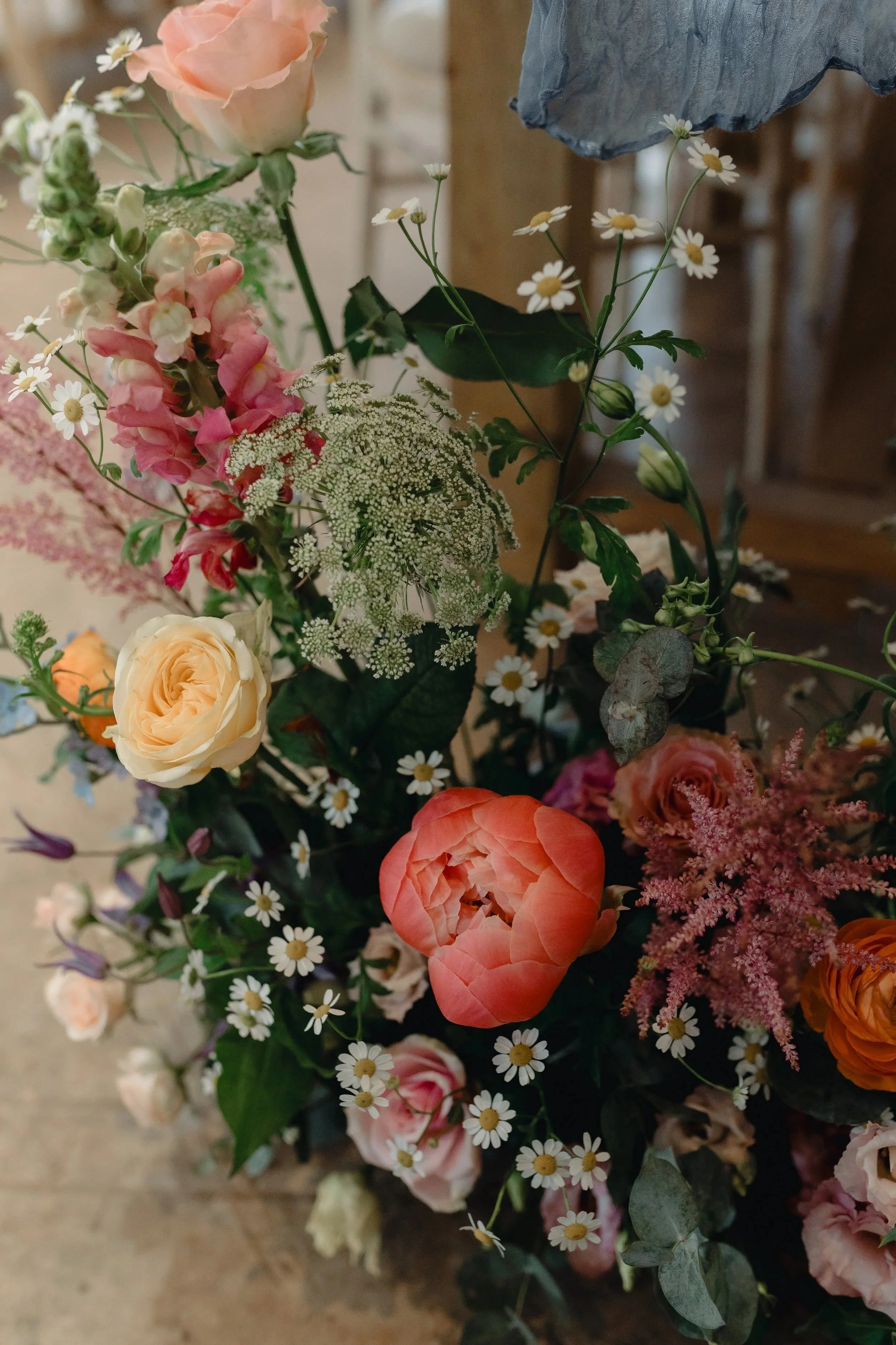 A colorful bouquet of flowers including pink, peach, white roses, white daisies, and small pink blossoms, set against a blurred background.