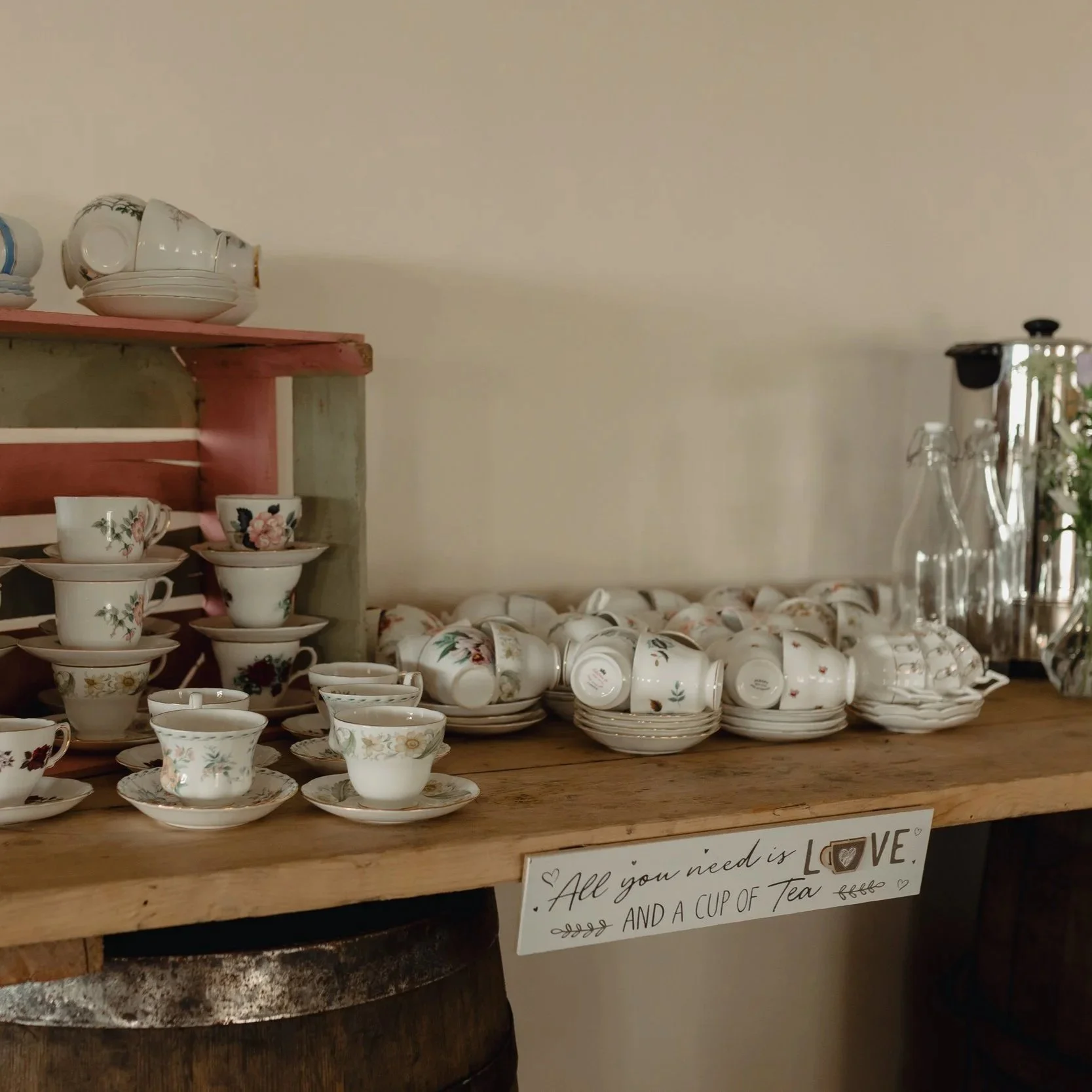 Display of stacked floral patterned teacups and saucers on a wooden shelf, with some teapots and glasses nearby.