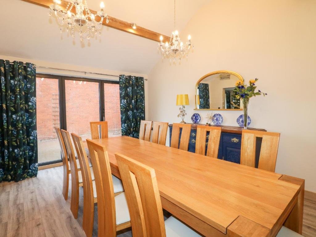 A dining room with a wooden table, nine matching chairs, a blue sideboard with decor, a mirror, a chandelier, and large sliding glass doors with patterned curtains.