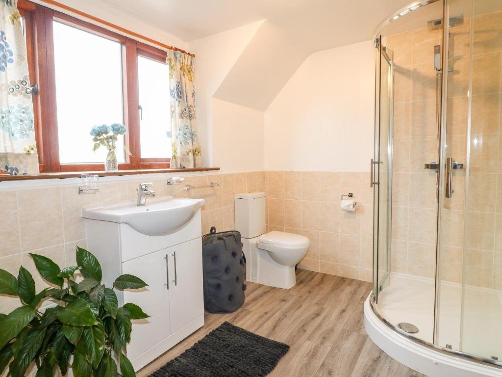 Bathroom with a window, curtain, sink with cabinet, toilet, shower with glass door, and a plant.