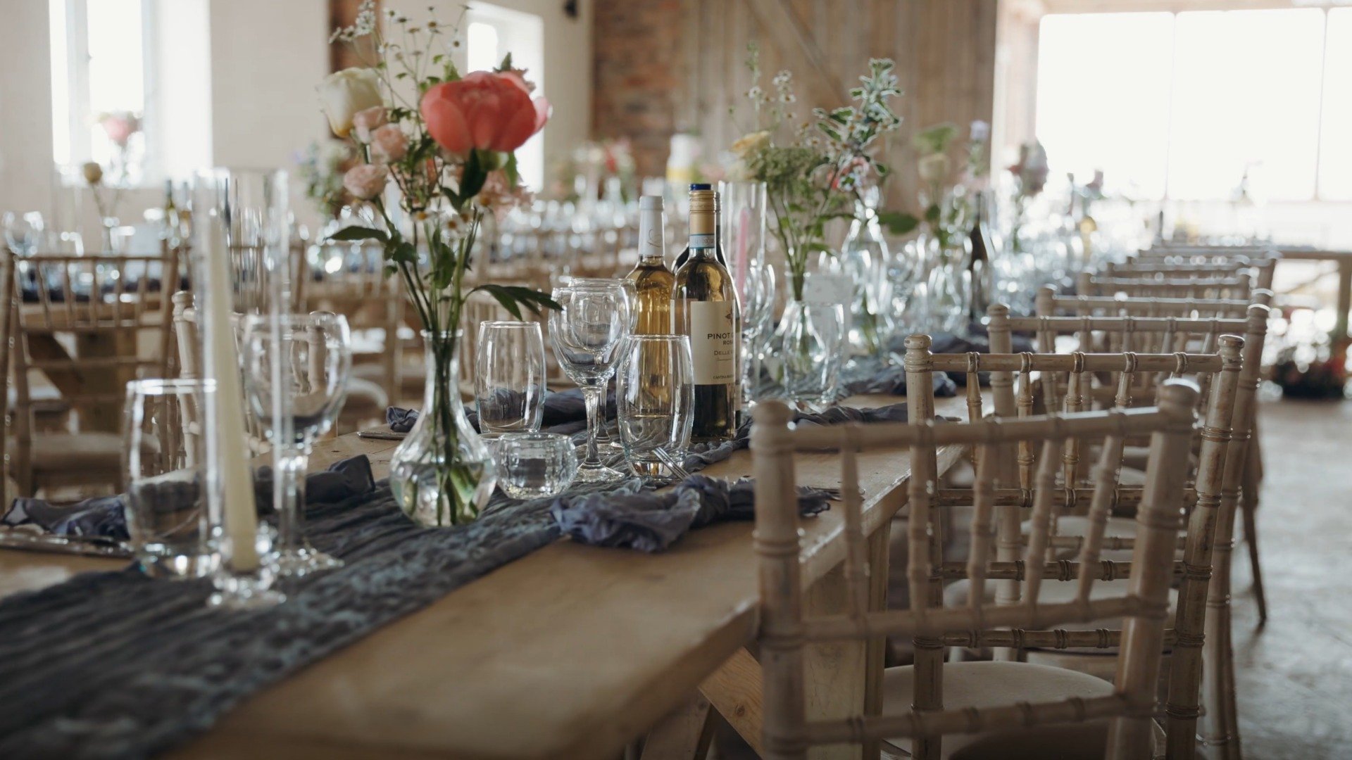 Decorated banquet table with floral centerpieces, wine bottles, and glassware in a bright, rustic venue.