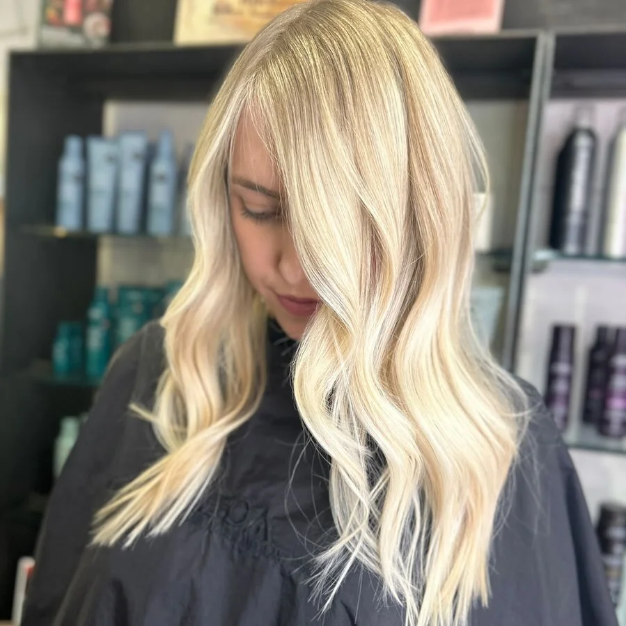 Young woman with long, wavy blonde hair in a salon setting.