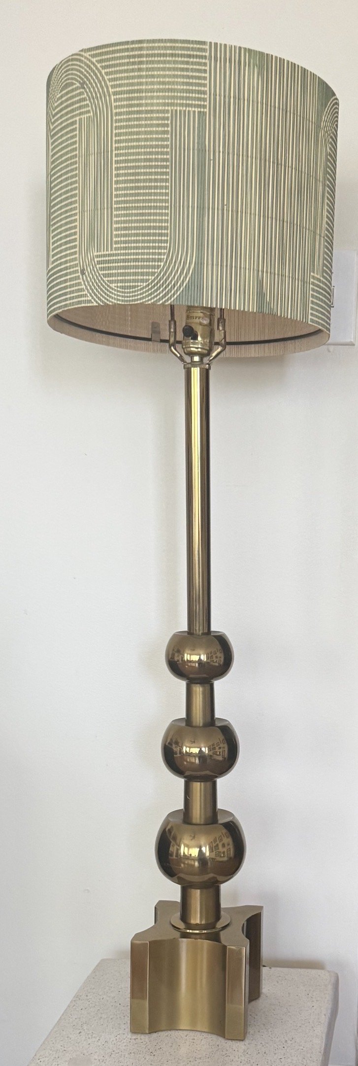 A commanding vintage table lamp in polished brass, distinguished by its architectural stacked-sphere column and geometric cruciform base. The graduated orb detailing along the stem gives the piece a sculptural presence that reads equally as decorativ