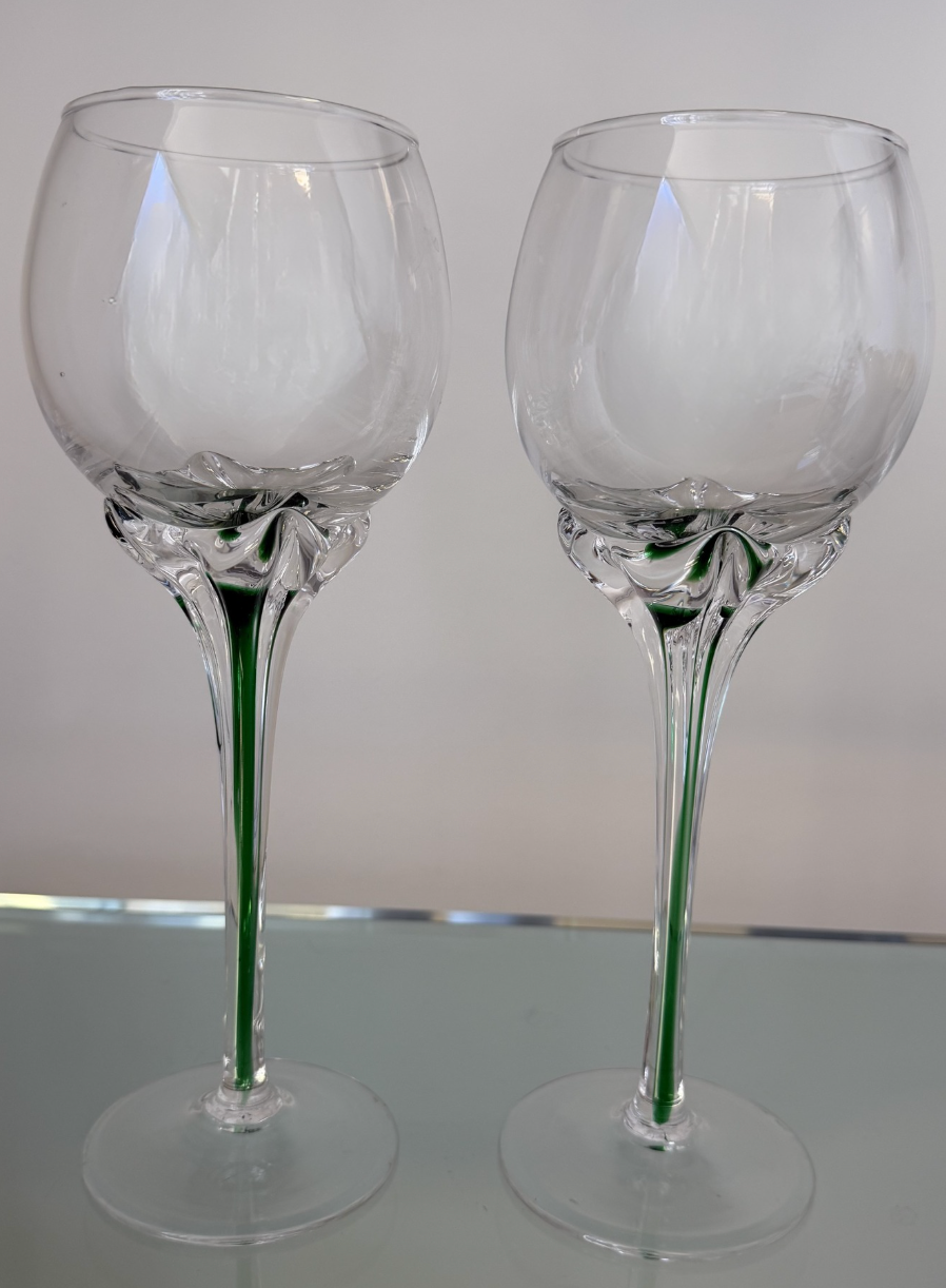 Elegant and sculptural in form, this pair of vintage wine glasses features an elongated silhouette with striking emerald green detailing suspended within clear glass, creating a subtle sense of movement and artistry. The dramatically tall stems lend 