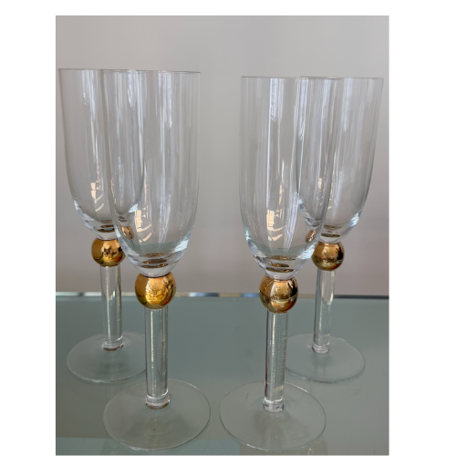 Graceful and understated, this vintage set of four champagne flutes features a clean elongated silhouette accented by luminous gold sphere detailing at the stem. The balance of clear glass and warm metallic tones gives the set a refined, timeless qua